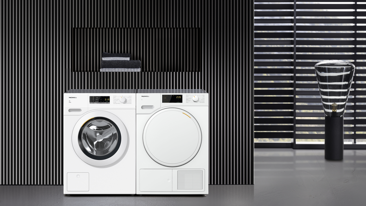 Biała pralka i suszarka Miele, z czarną ścianą lamelową i lampą.