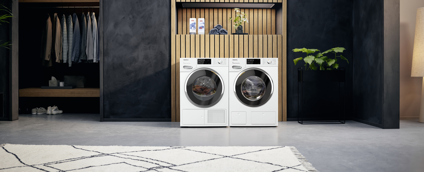 Biała pralka i suszarka w pokoju z drewnem i roślinami.