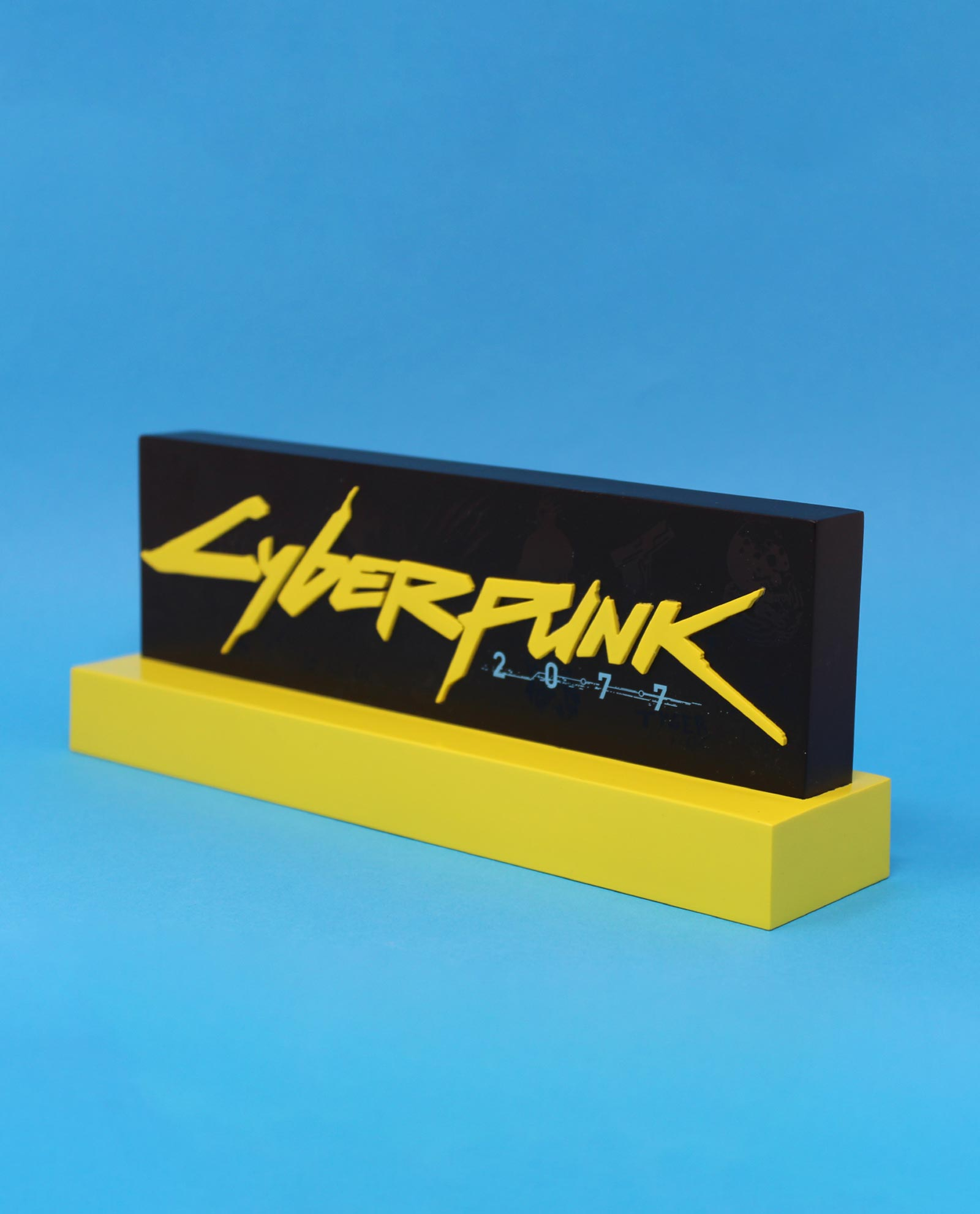 Ein Cyberpunk 2077 Logo auf einem schwarzen Block mit gelbem Sockel. Der Hintergrund ist blau.