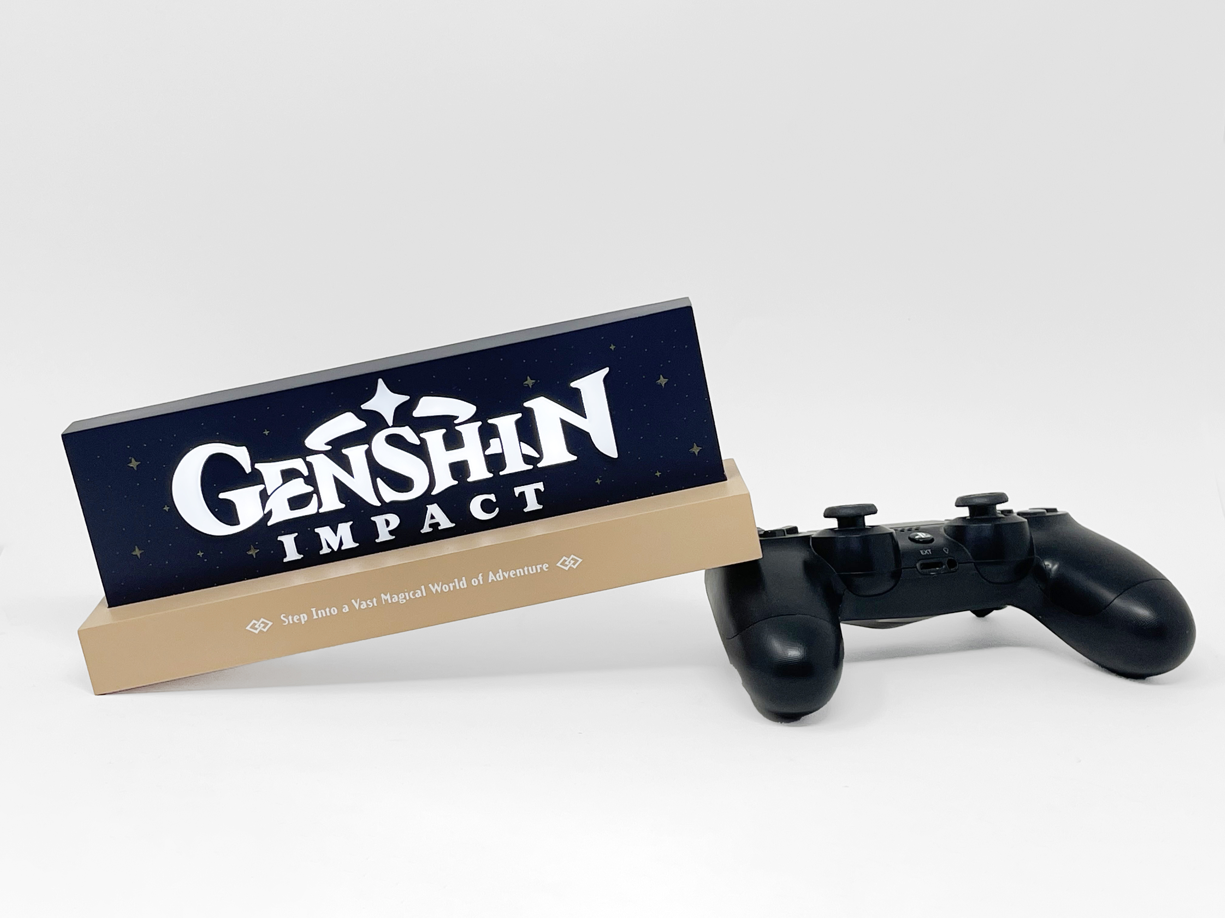 Ein Genshin Impact Schild und ein schwarzer PS4-Controller auf weißem Grund.