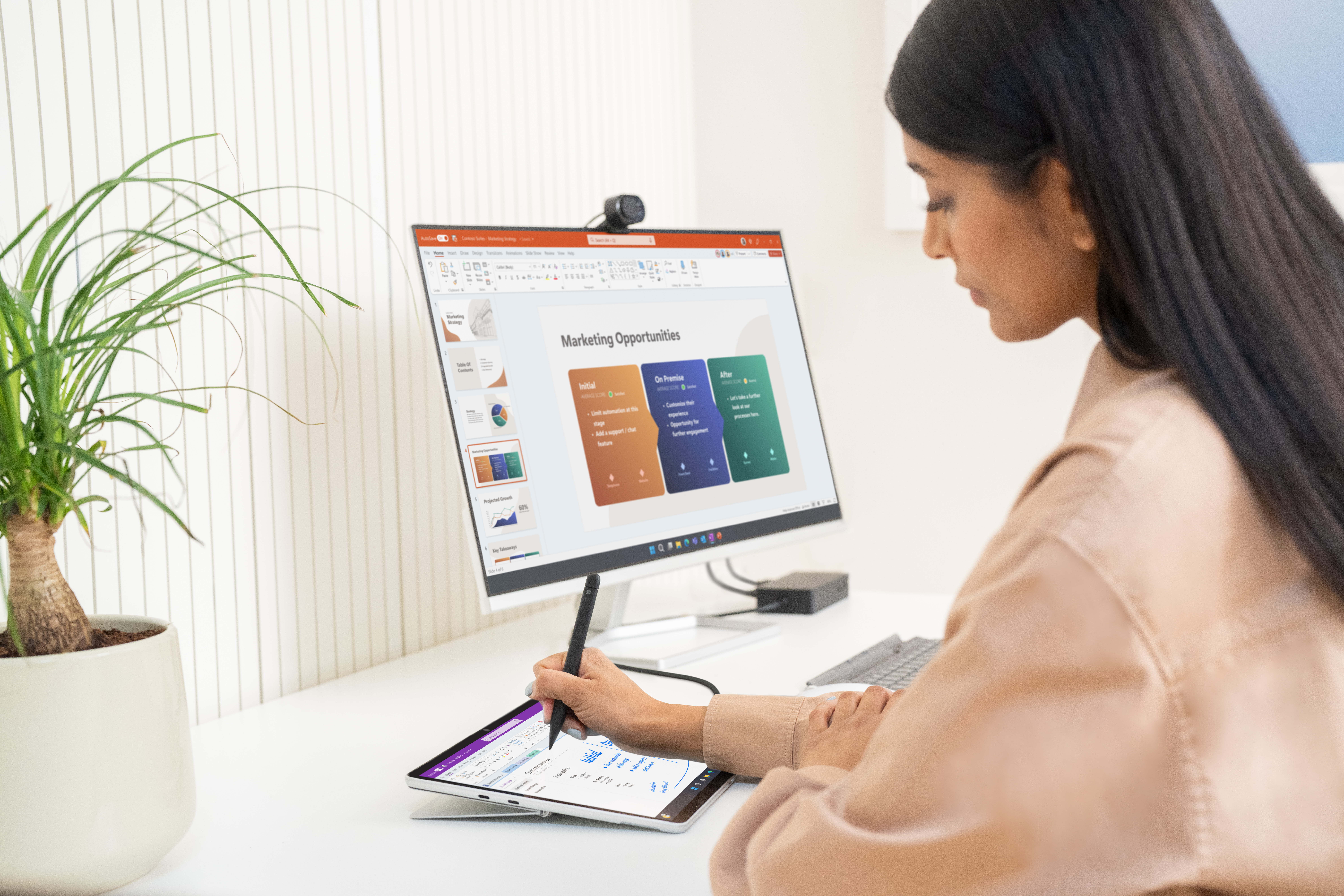 Vrouw die op een bureau werkt met monitor, tablet en presentatie, schrijft met een stylus.