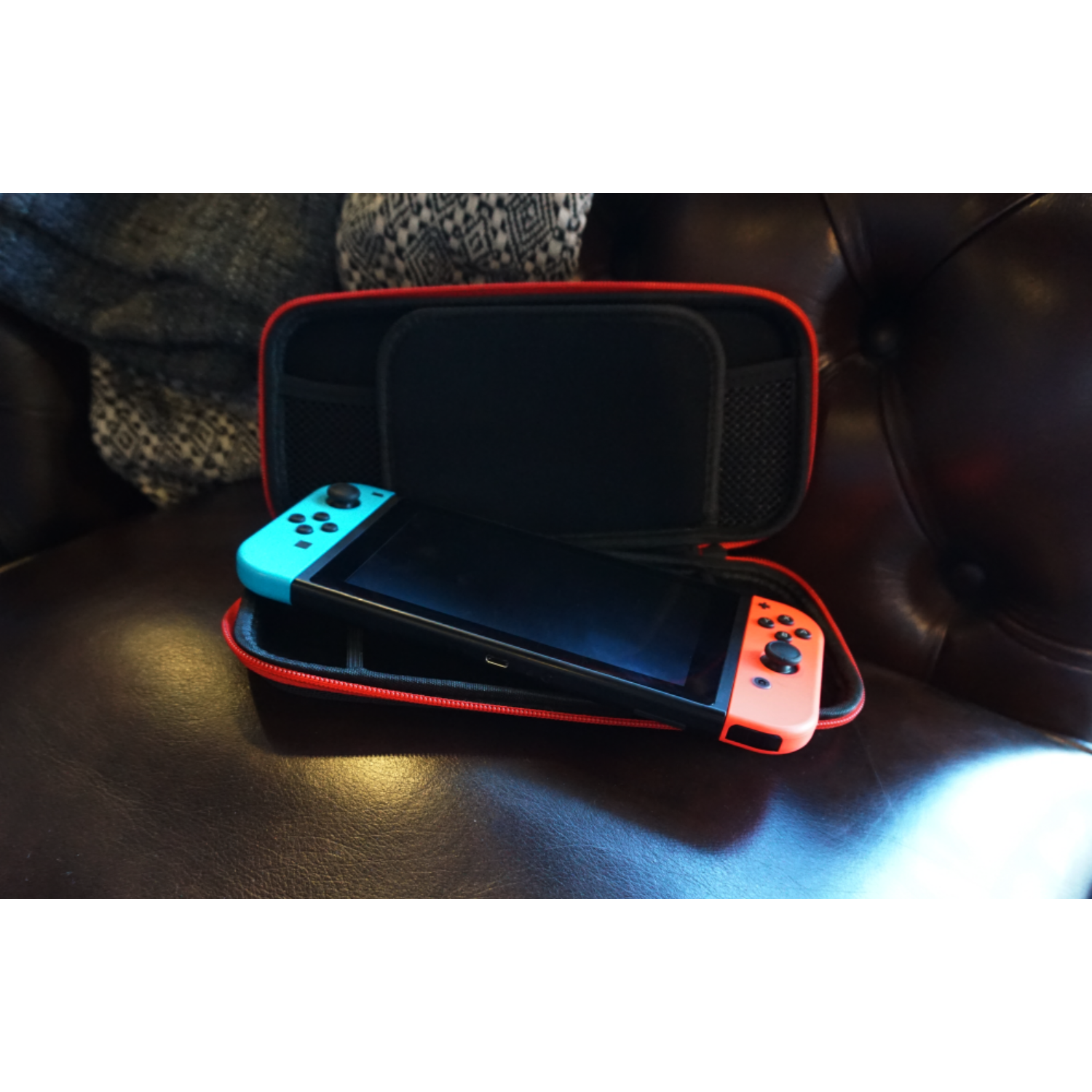 A Nintendo Switch console with controllers, inside a red and black carrying case, on a brown surface.