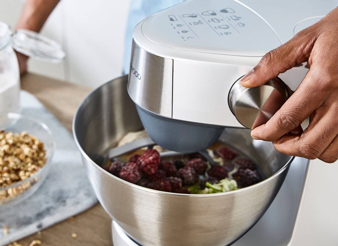 Ręka osoby używa pokrętła na misce miksera, w otoczeniu kuchni.