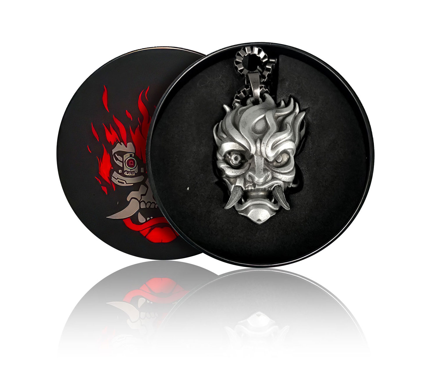 Srebrny wisiorek w kształcie maski demona w czarnym pudełku z czerwonymi akcentami, otoczony opakowaniem.