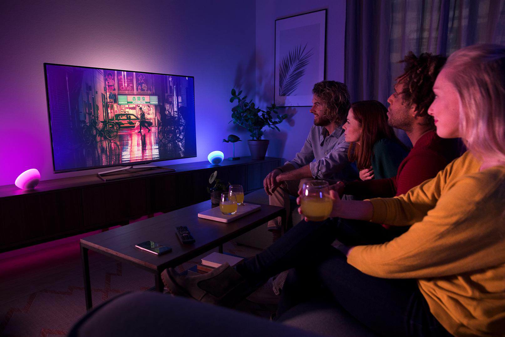 Gruppe von Leuten, die im Wohnzimmer fernsehen. Der Fernseher zeigt eine bunte Stadtszene.