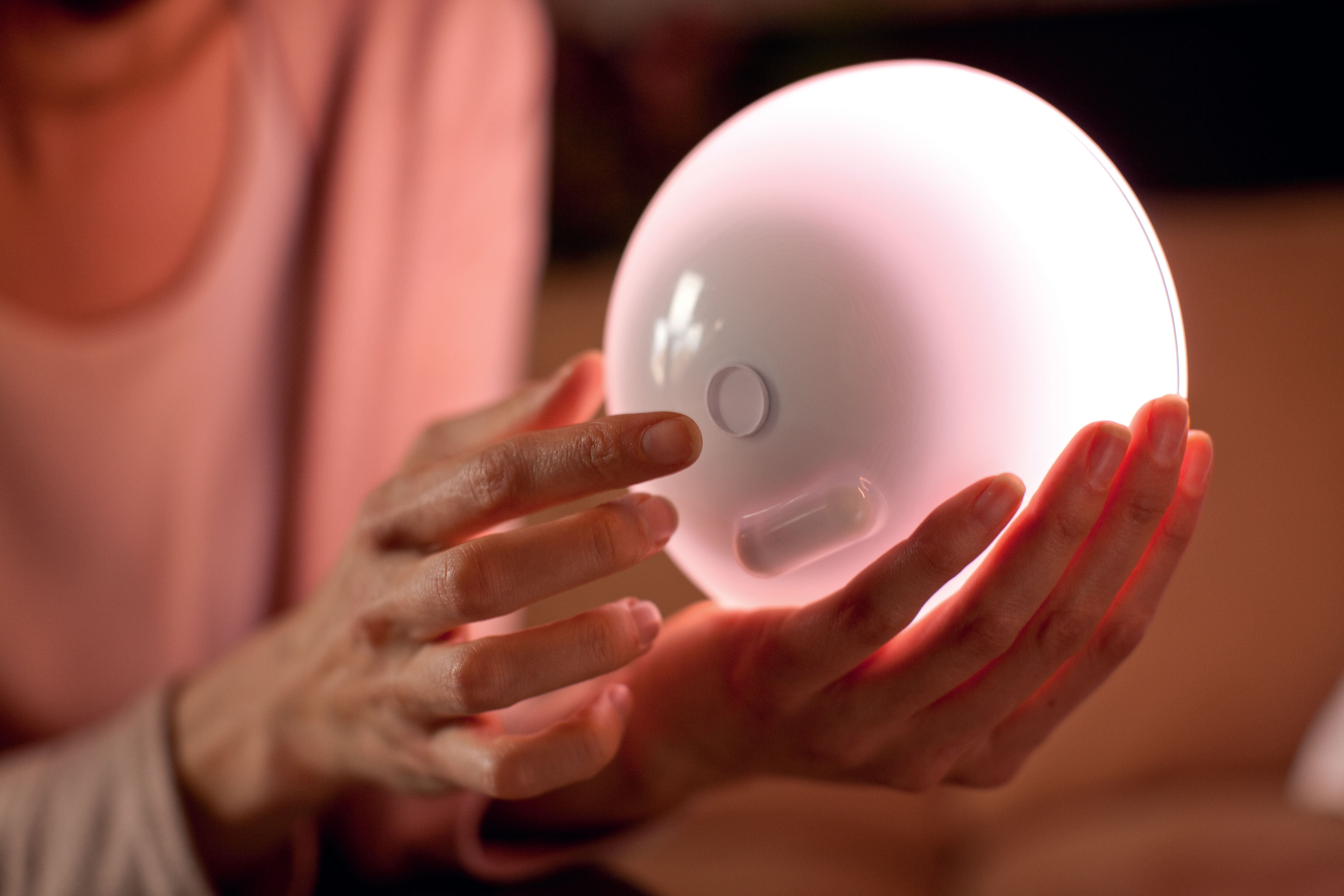 Eine weiße Smart-Lampe in Händen gehalten. Das Licht ist an und rosa.