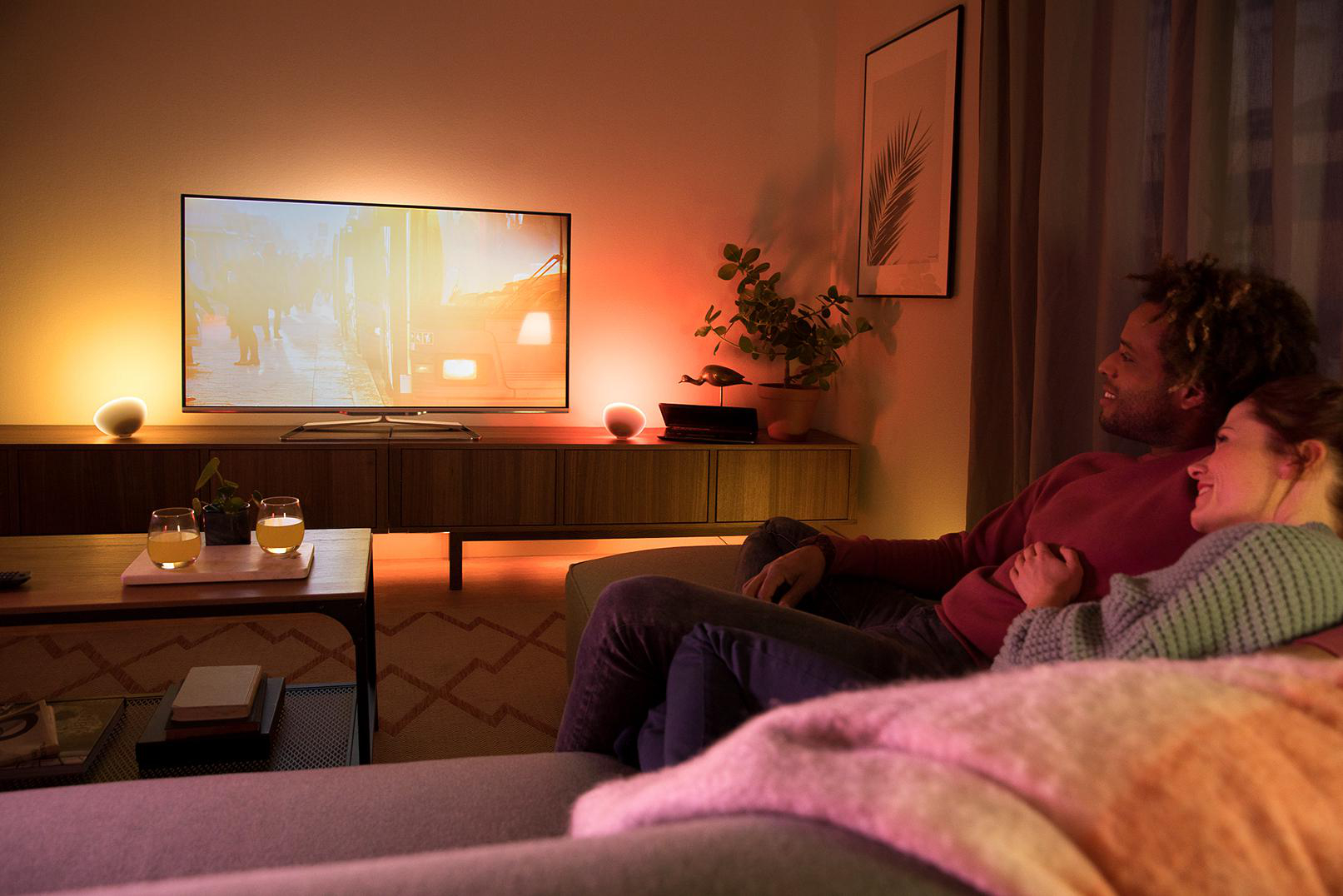 Ein gemütliches Wohnzimmer mit Fernseher, Paar auf dem Sofa und Umgebungslicht.