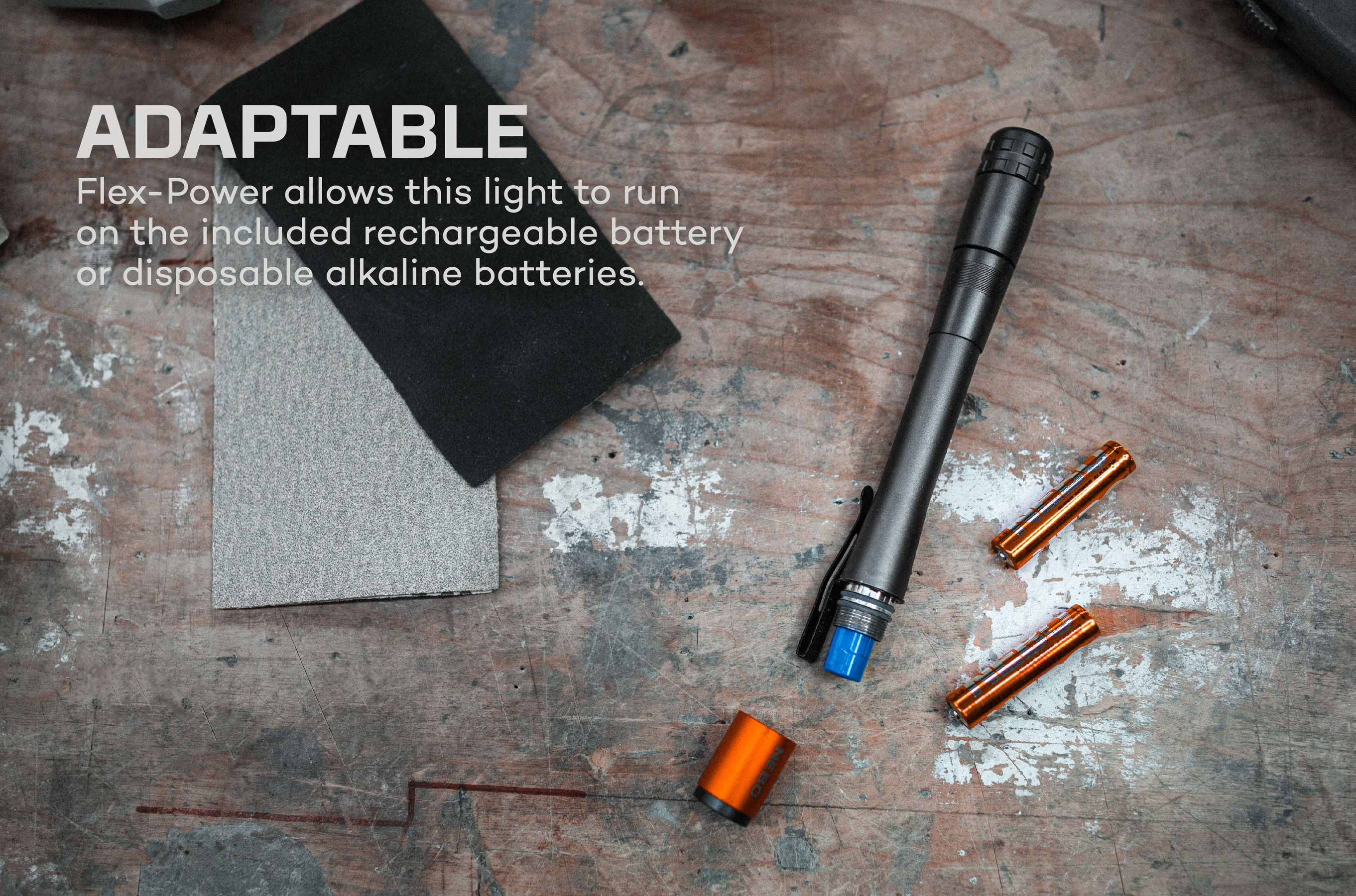 Eine Taschenlampe mit blauem Ende und einer orangefarbenen Endkappe, neben Schleifpads und Batterien.
