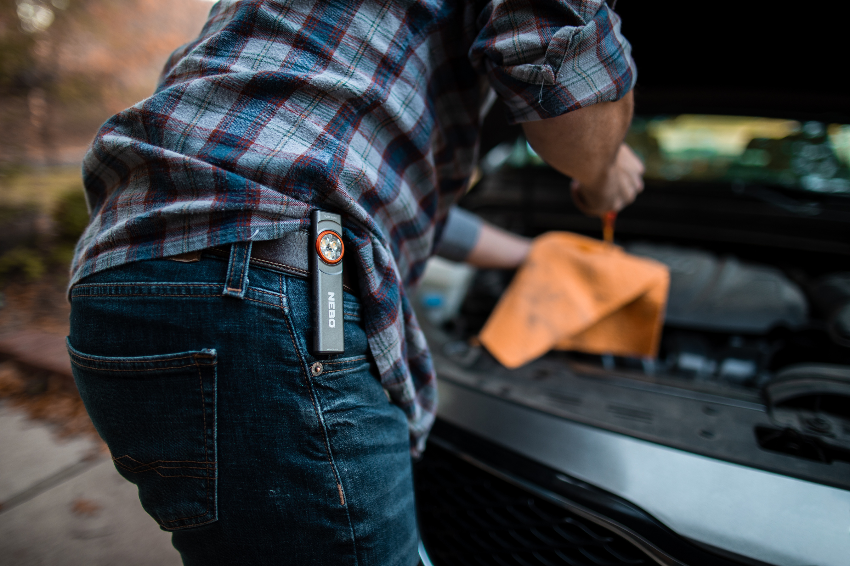 Ein Mann in Jeans und einem karierten Hemd mit einer Taschenlampe in der Tasche arbeitet an einem Auto.