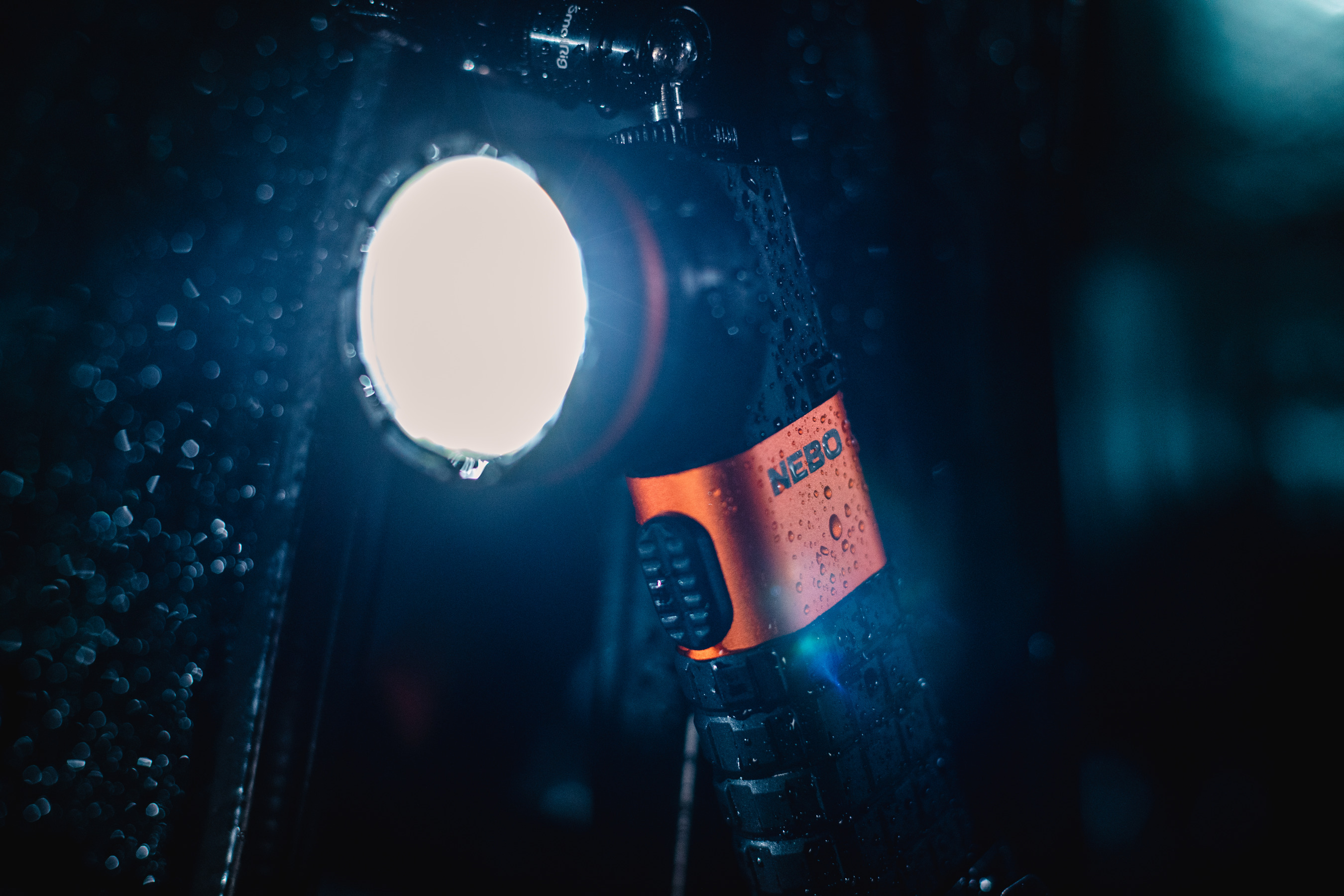 Eine Taschenlampe ist beleuchtet und nass mit Wassertröpfchen. Die Taschenlampe ist schwarz mit einem orangefarbenen Band.