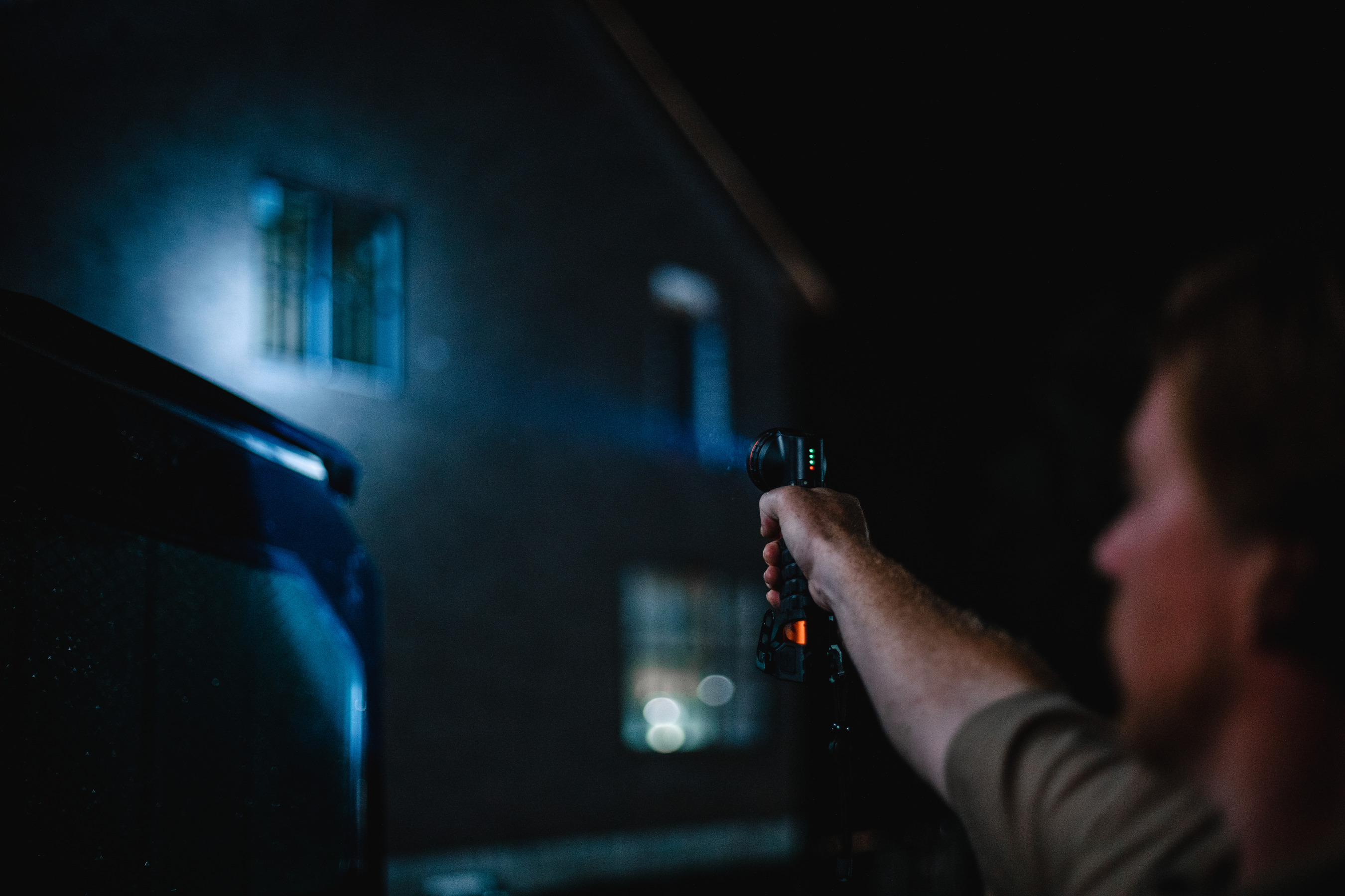Eine Hand, die eine Taschenlampe hält und nachts auf ein Gebäude zeigt.
