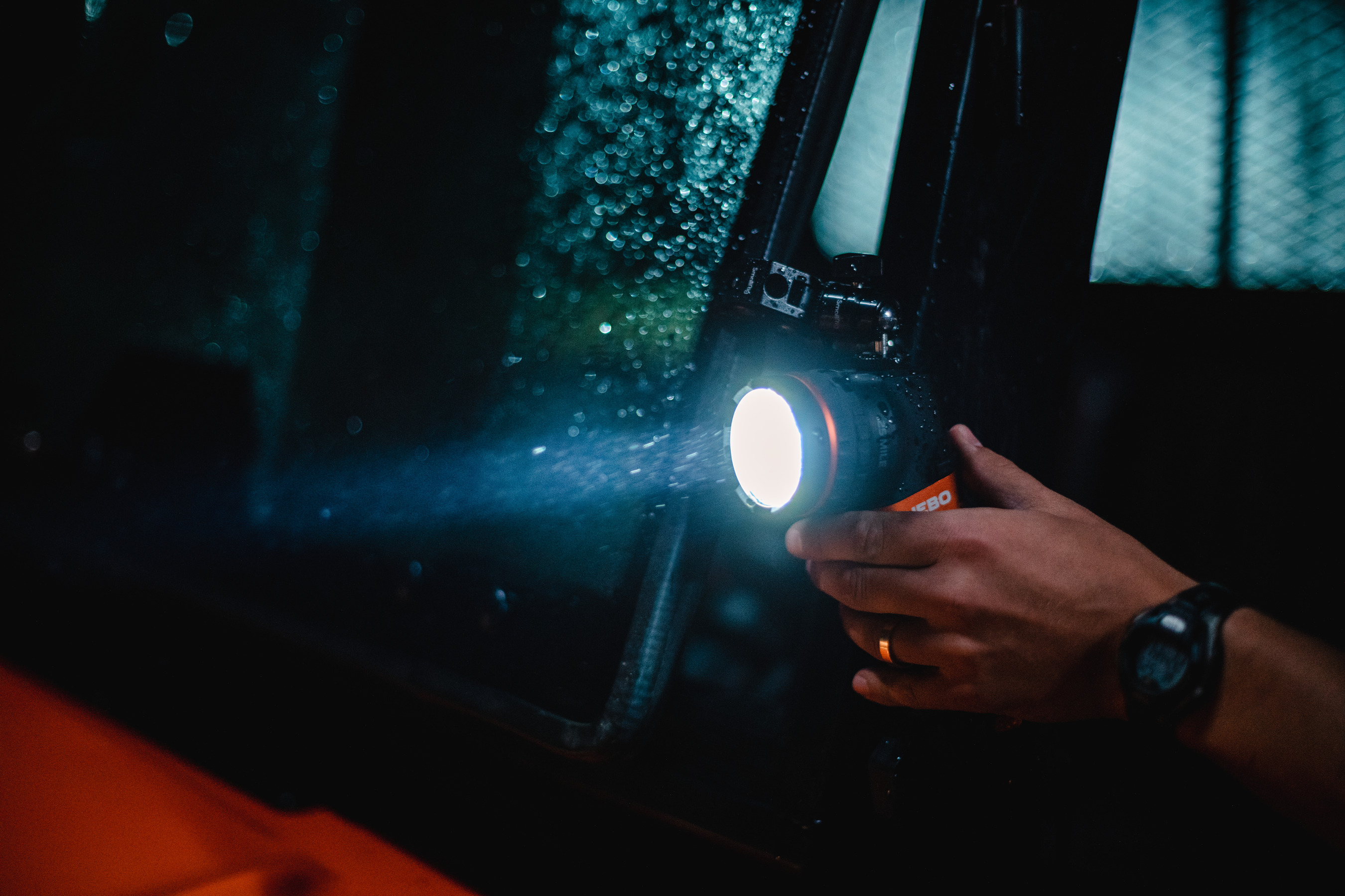 Person hält Taschenlampe im Regen bei Nacht, Lichtreflexion vom Fenster.