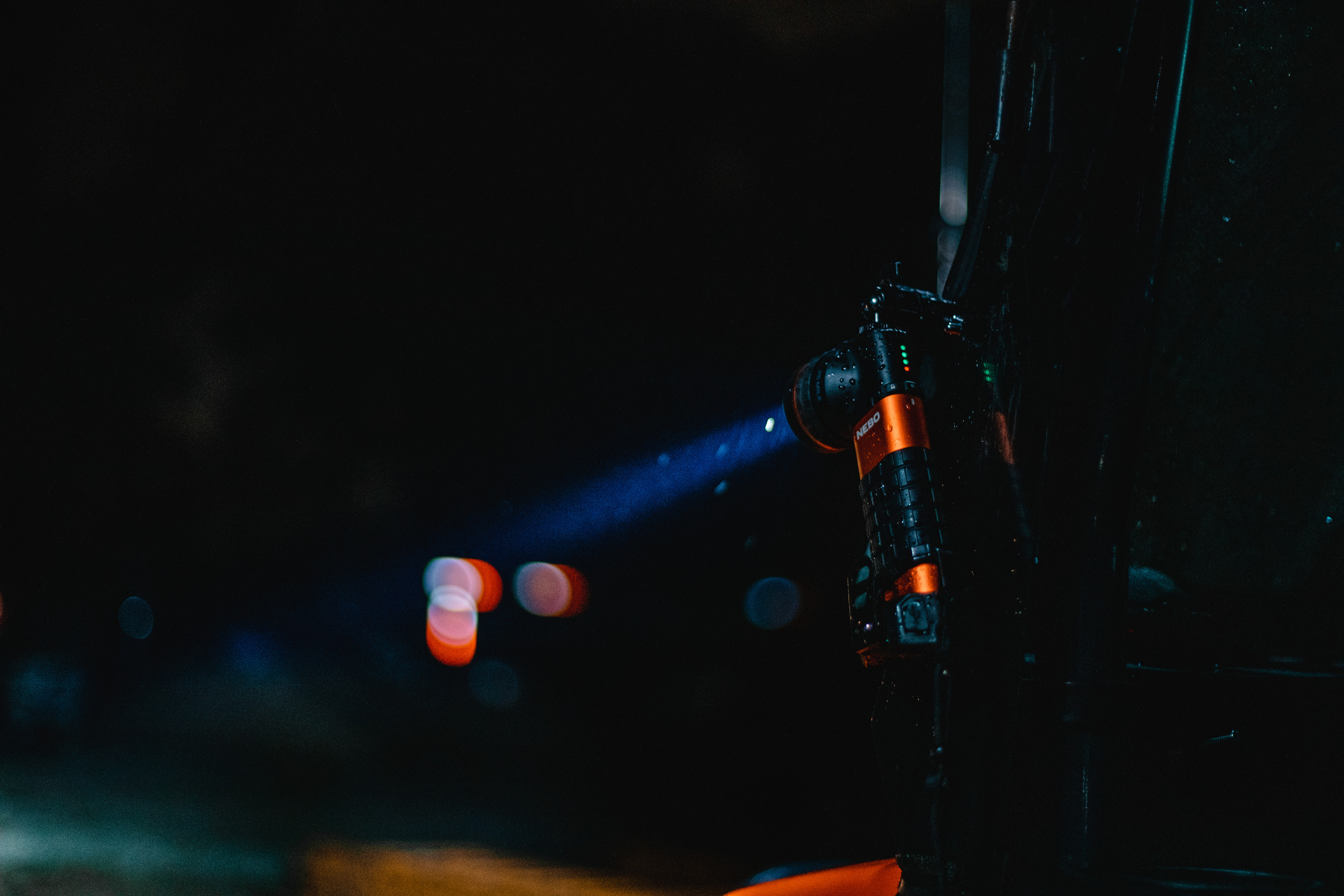 Eine hellorangefarbene und schwarze Taschenlampe, die einen Lichtstrahl in die Dunkelheit scheint, an einer Oberfläche befestigt.