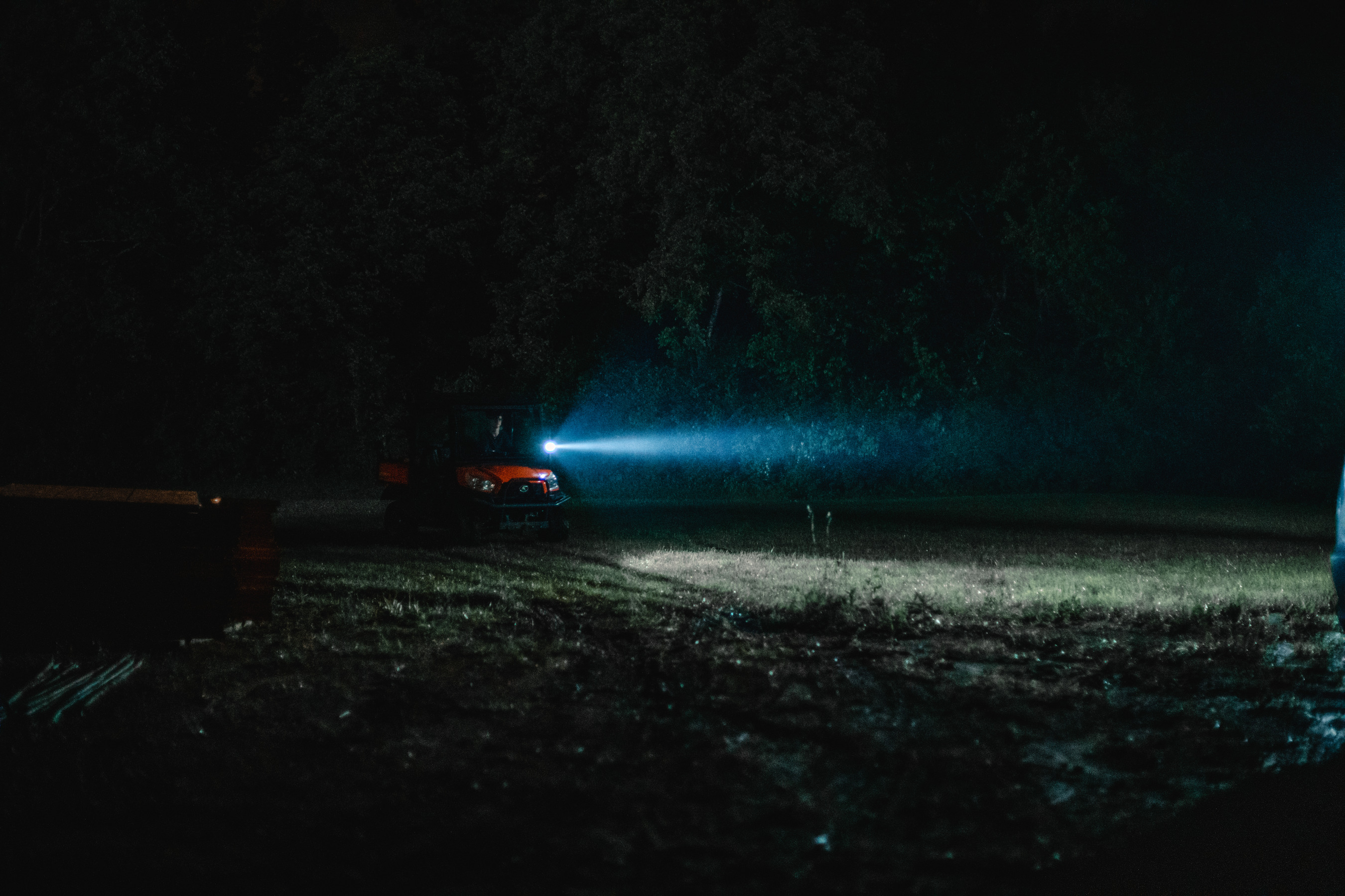 Ein Fahrzeug mit eingeschaltetem Scheinwerfer bei Nacht auf einem dunklen Feld. Der Lichtstrahl ist sichtbar.