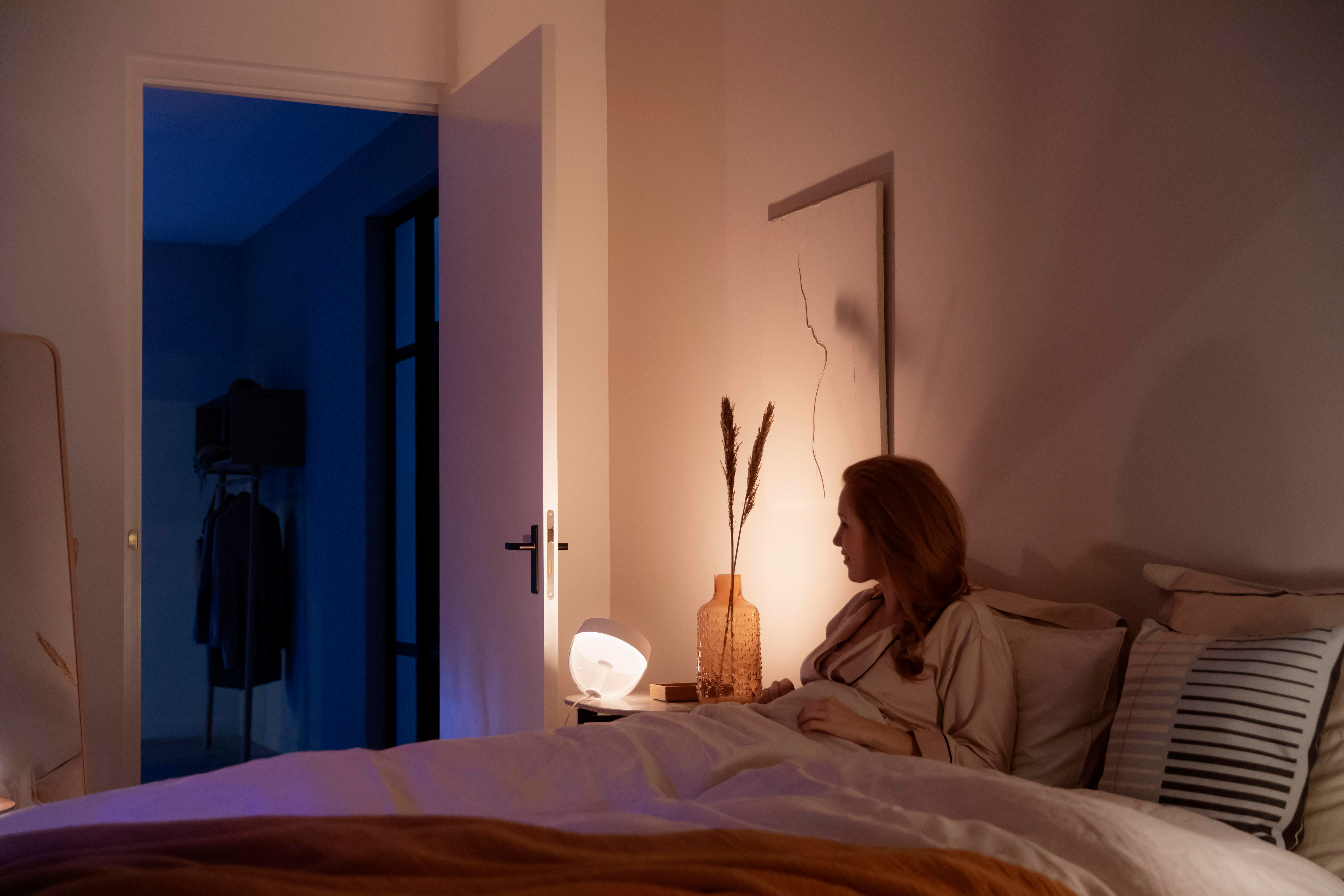 Eine Frau sitzt auf dem Bett in einem Schlafzimmer mit sanfter Beleuchtung.
