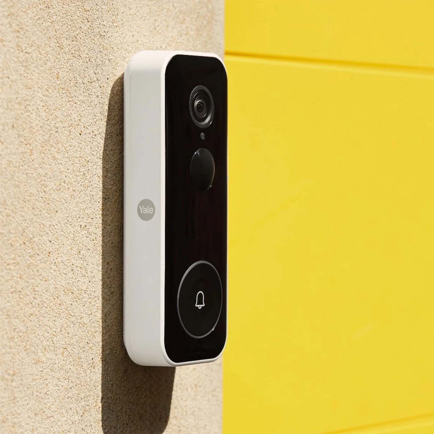 Un campanello Yale bianco e nero è montato su un muro beige, con uno sfondo giallo brillante.
