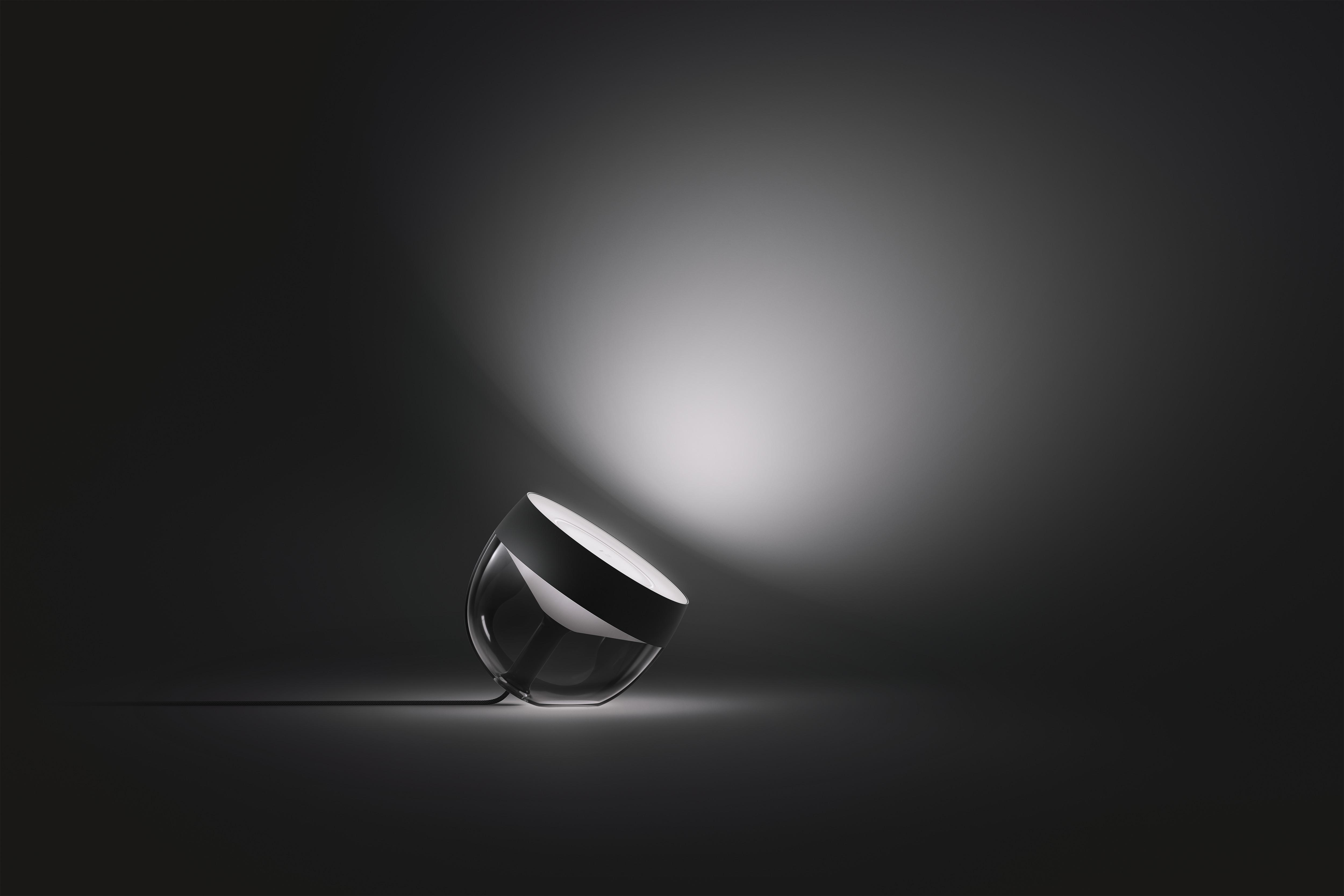 Eine moderne Lampe mit schwarzem Oberteil und transparentem Sockel, auf dunklem Grund.