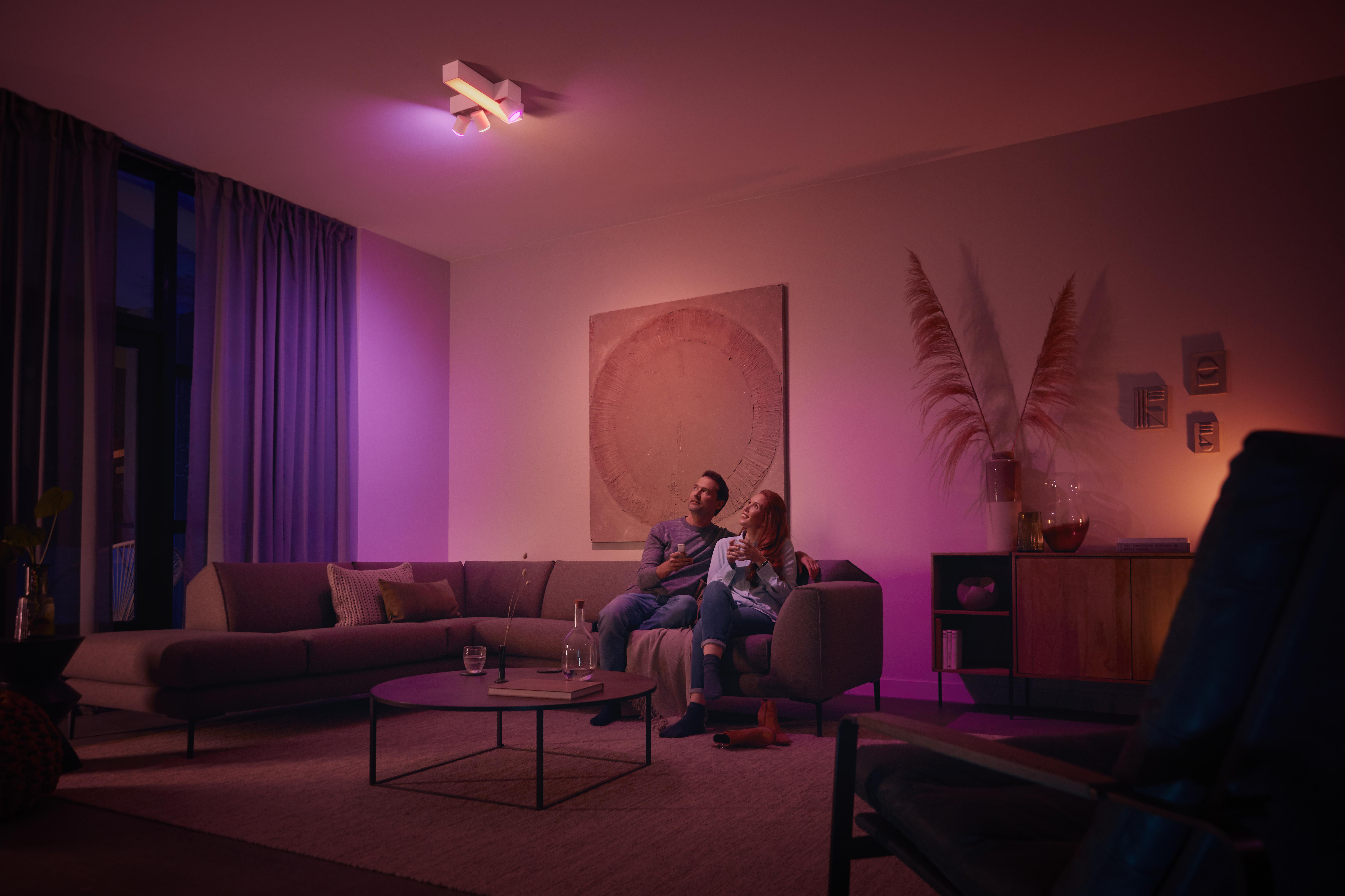 Wohnzimmerszene bei Nacht mit einem Paar, das sitzt, beleuchtet von bunten Smart-Leuchten.