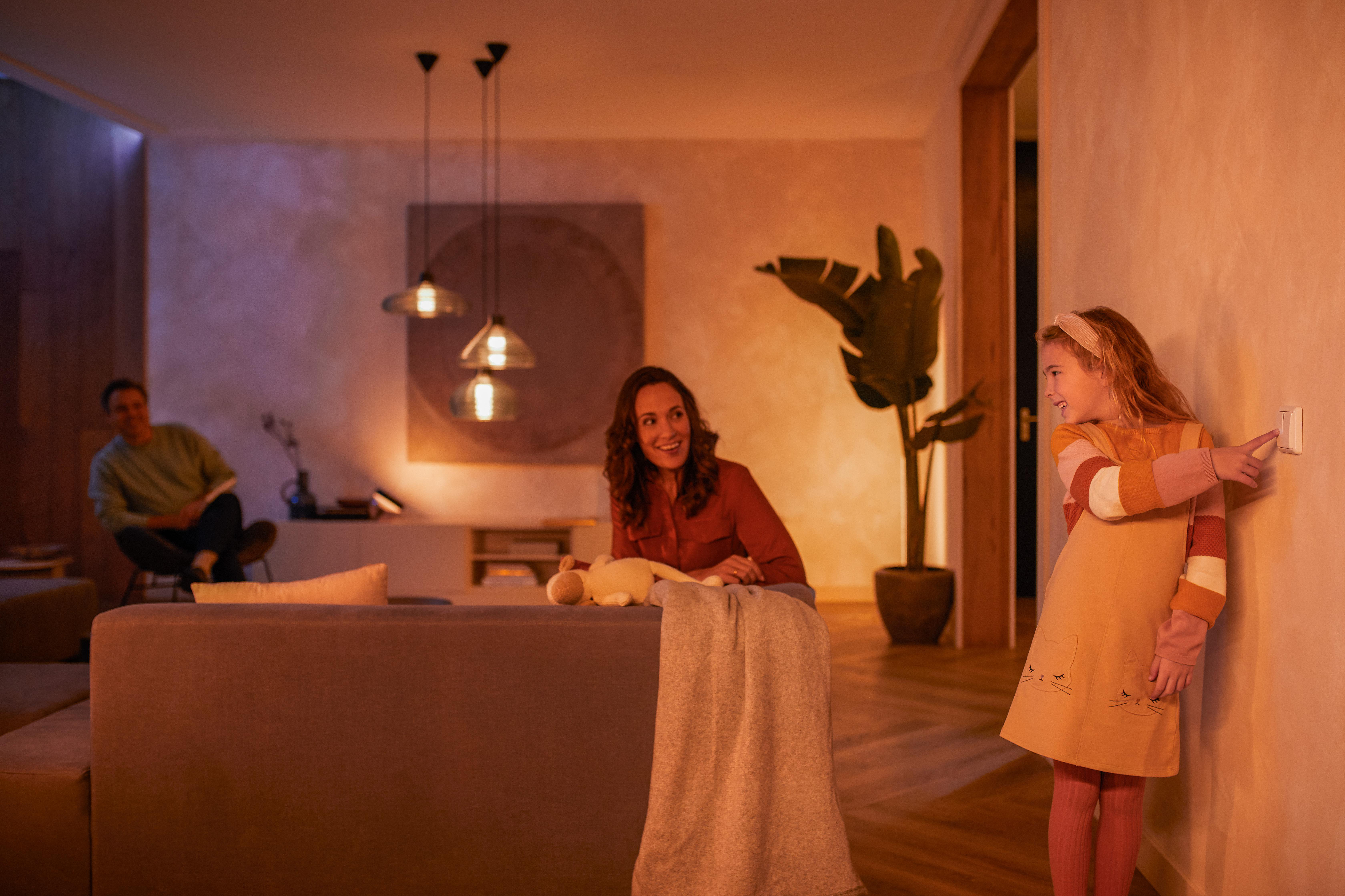Eine Familie in einem modernen Wohnzimmer, ein Mädchen berührt einen Lichtschalter.