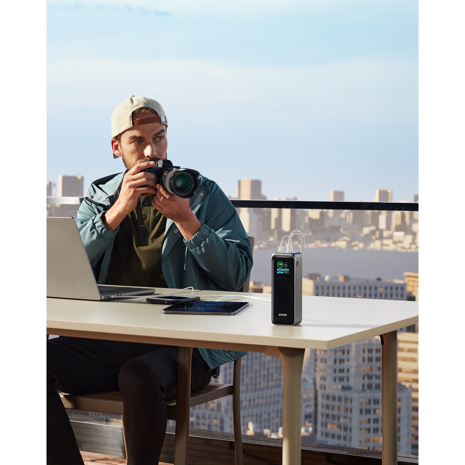 Homme sur balcon prend photo avec appareil, ordinateur portable et batterie externe.