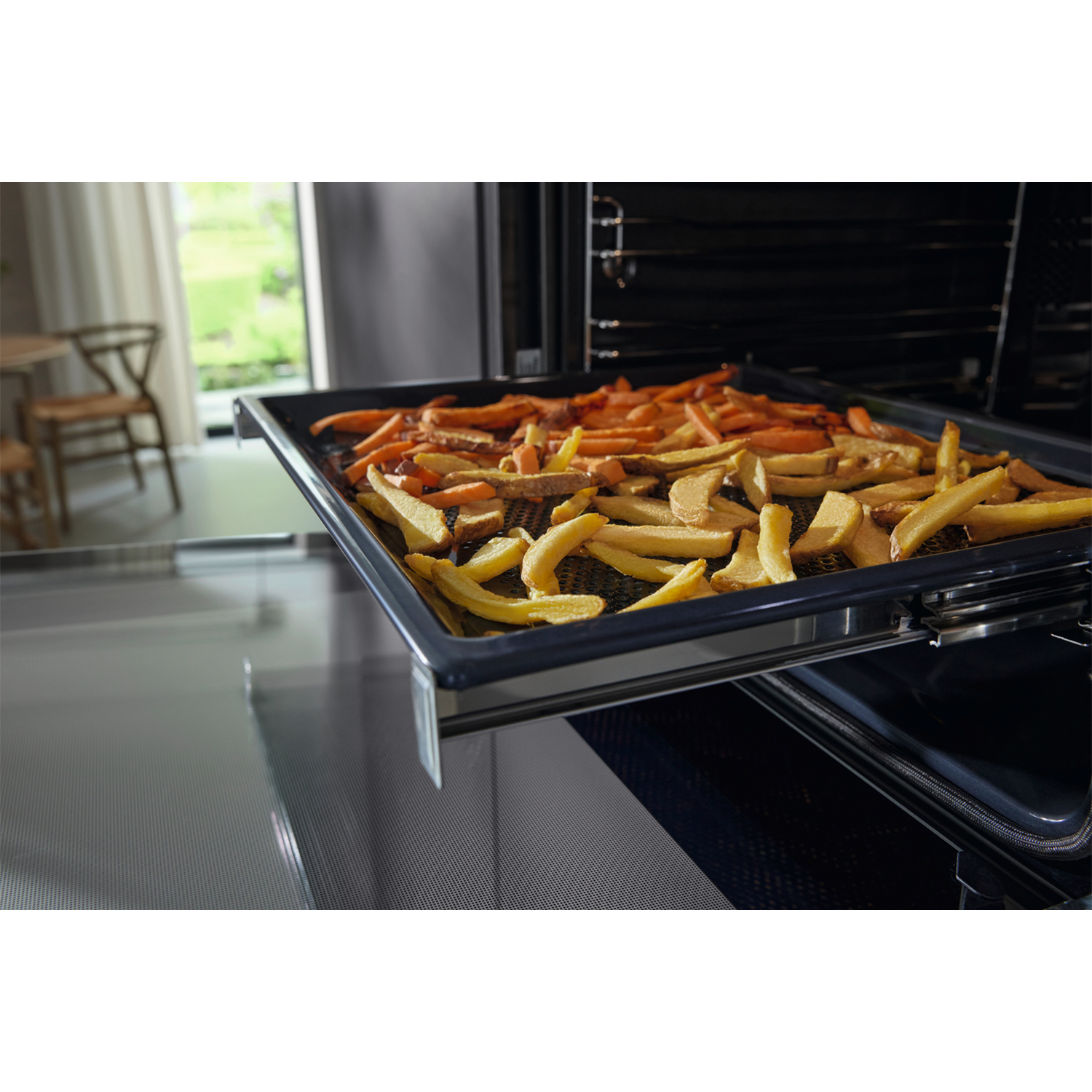 Vassoio di patatine fritte e carote in un forno, parzialmente estratto.