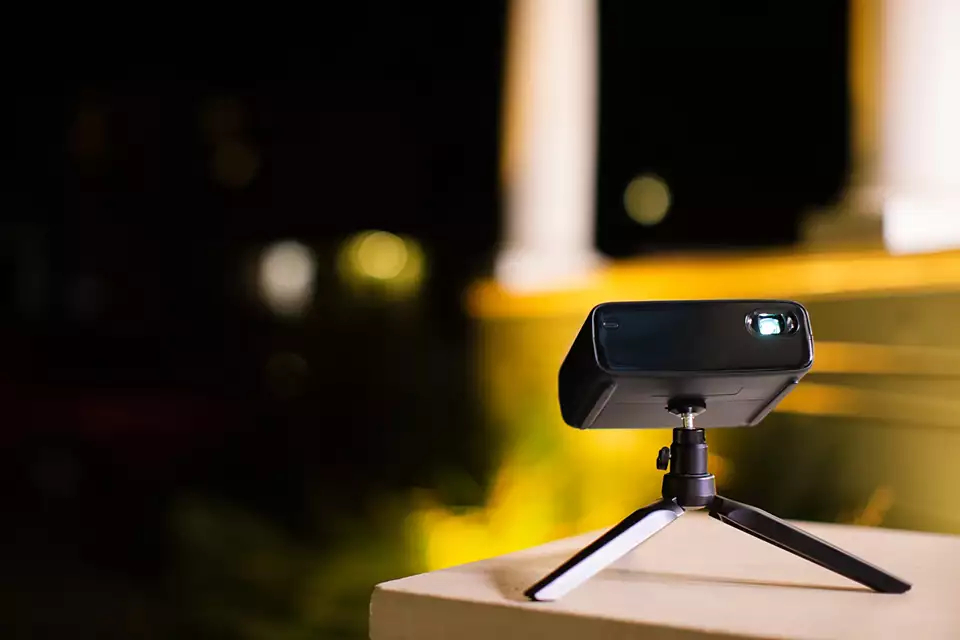 Mały czarny projektor na statywie, rzucający niebieskie światło na rozmyte tło.