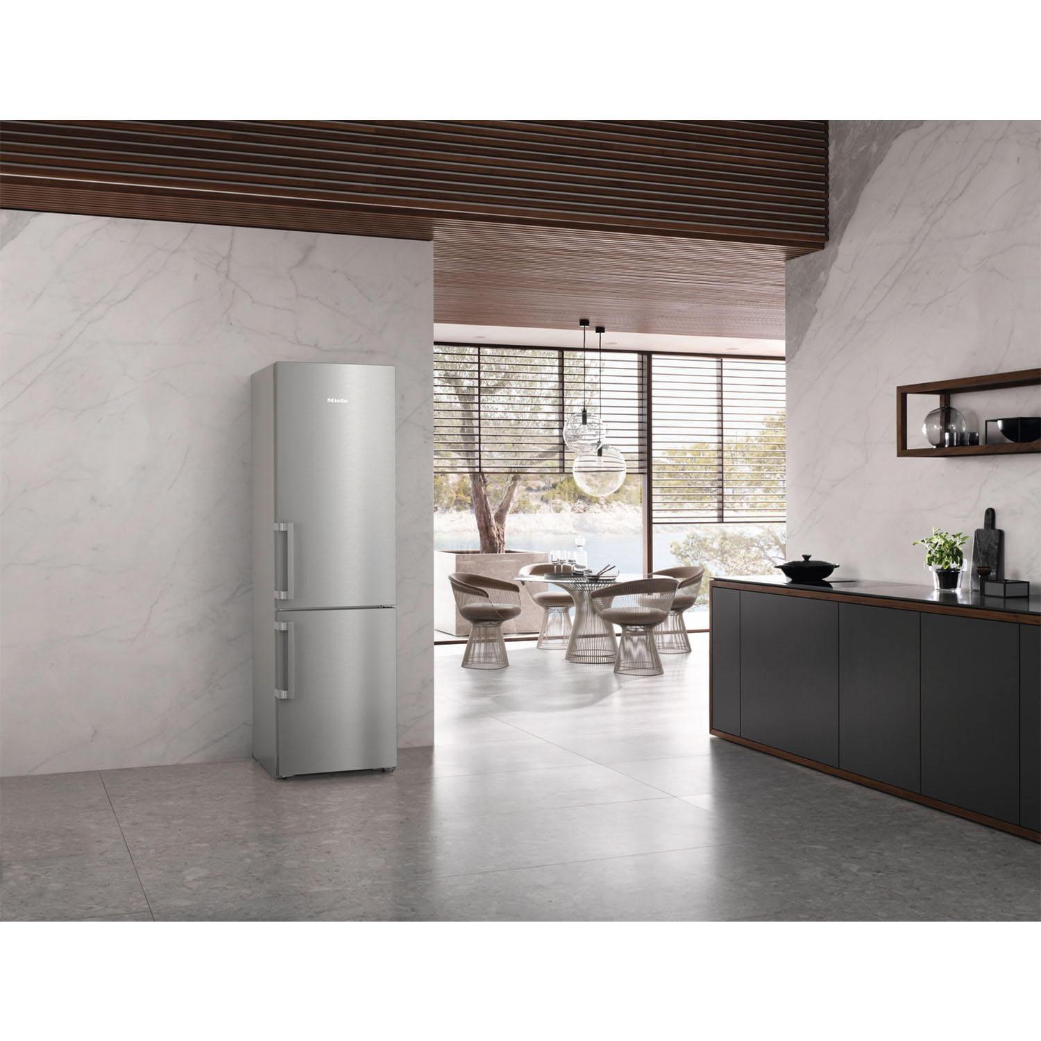 Frigorifero in acciaio inox in una cucina moderna. Muri bianchi, grandi finestre e bancone scuro.
