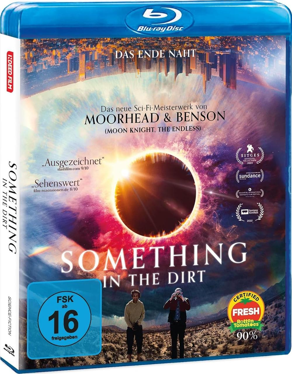 Blu-ray-Cover für 'Something in the Dirt'. Zeigt ein himmlisches Ereignis mit zwei Männern im Vordergrund.