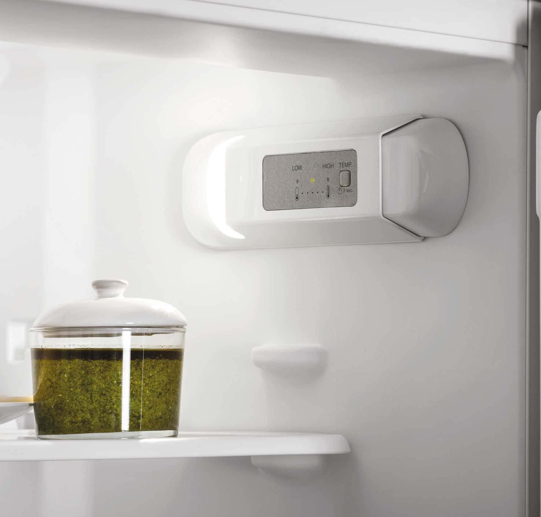 In einem weißen Kühlschrank: ein Glasgericht mit grünem Essen und Temperaturreglern oben.