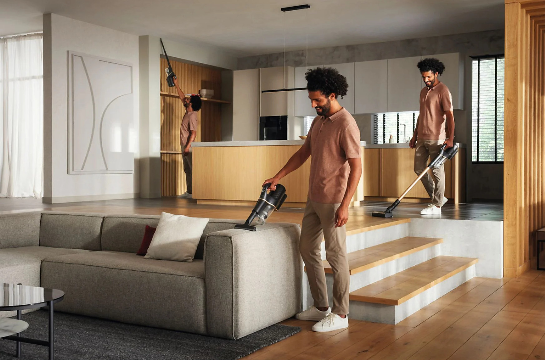 Mężczyzna używa odkurzacza na sofie. Druga postać w tle. Nowoczesne wnętrze.