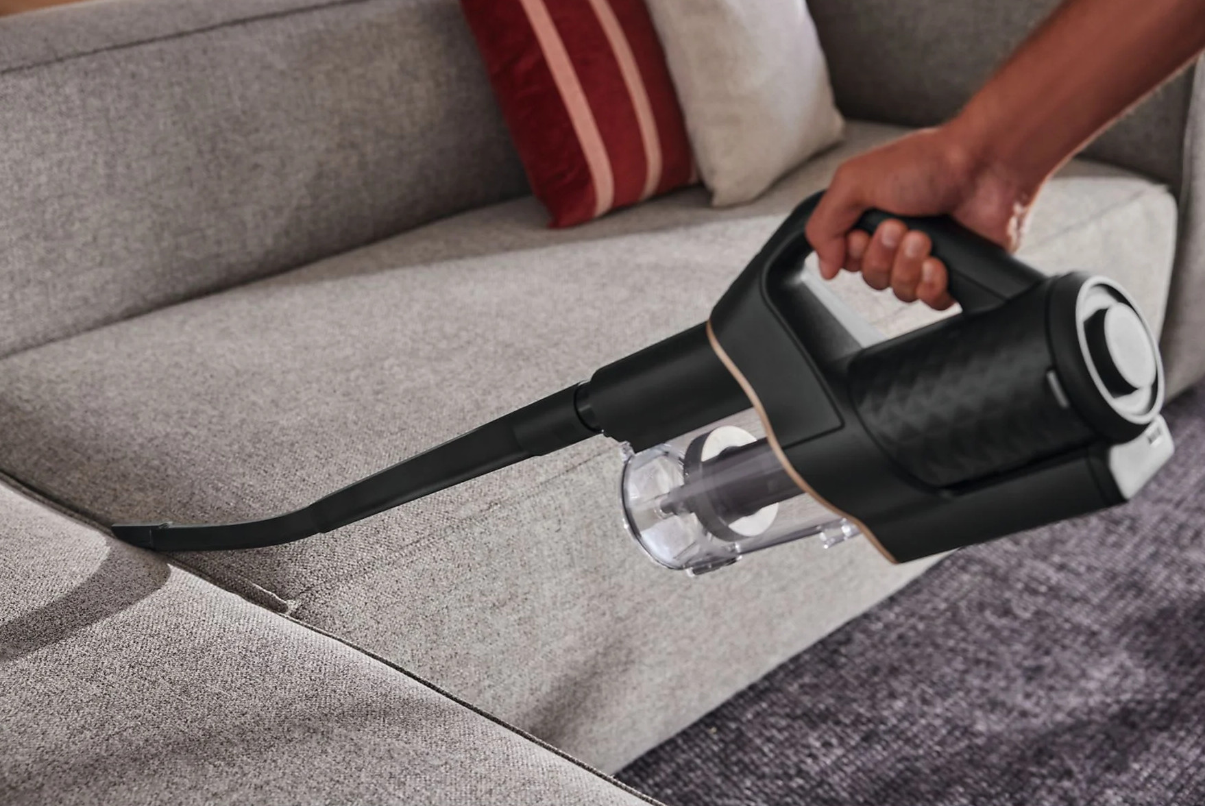 Osoba czyszcząca sofę czarnym odkurzaczem ręcznym.