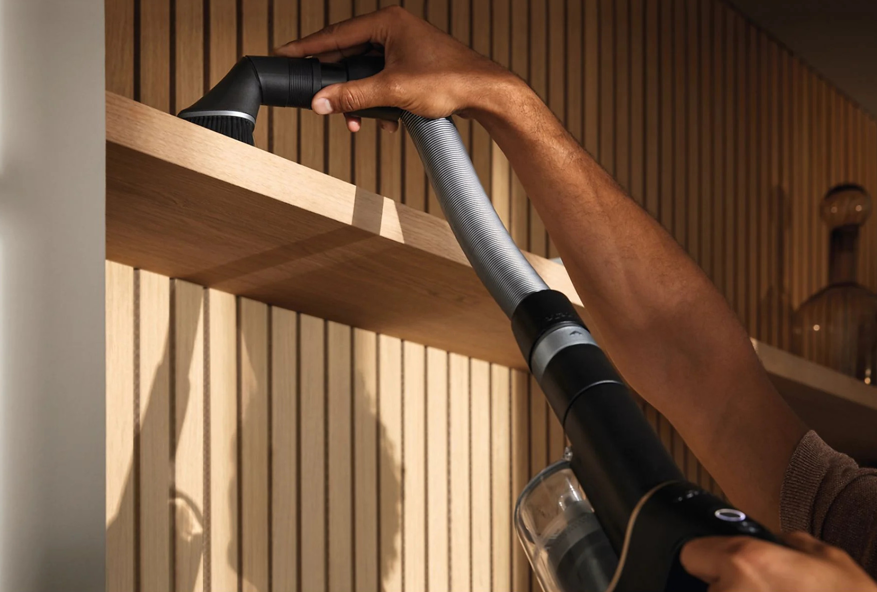 Osoba czyszcząca drewnianą półkę odkurzaczem.