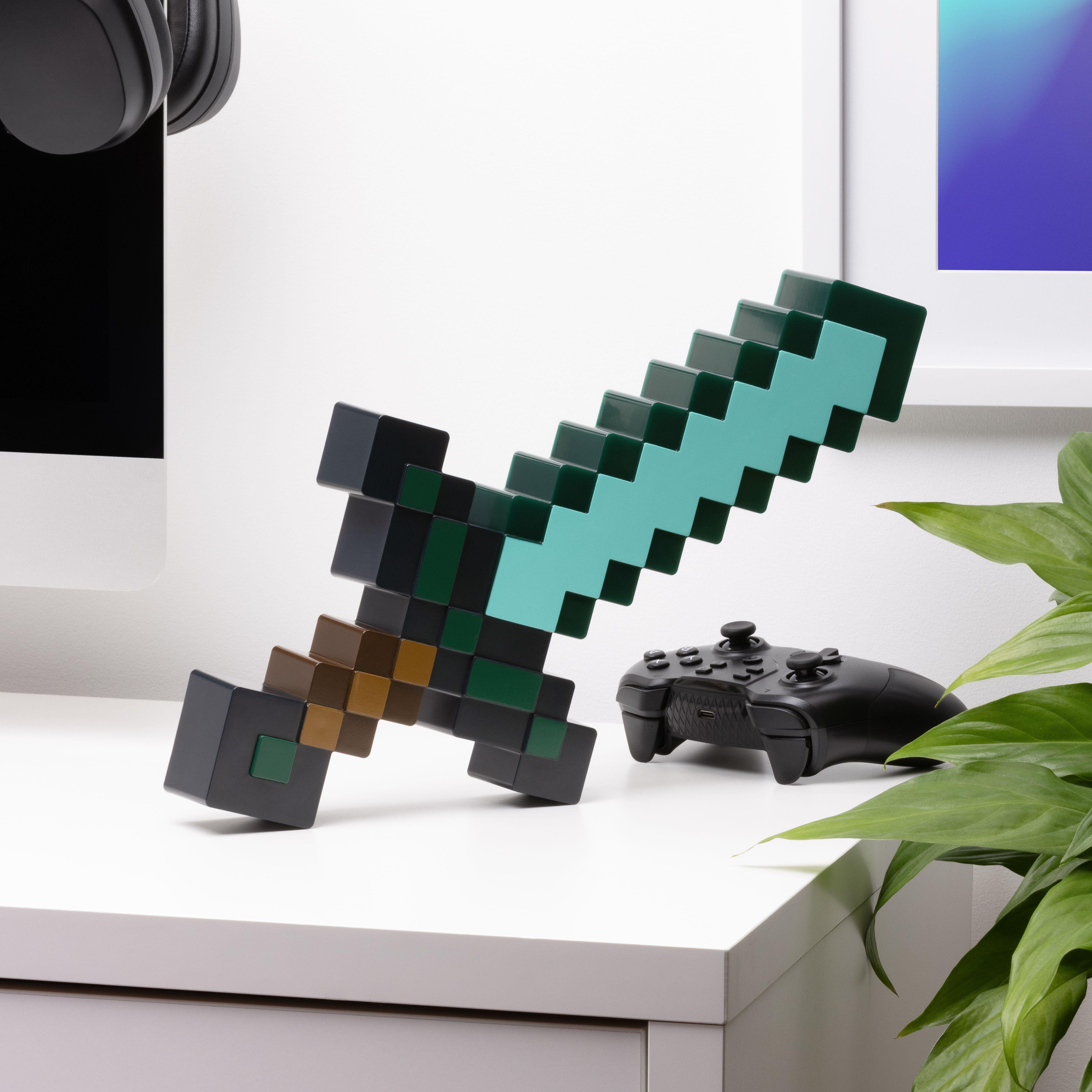 Ein Minecraft-Schwert und ein Gamecontroller liegen auf einem weißen Tisch mit einer Pflanze und einem Monitor.