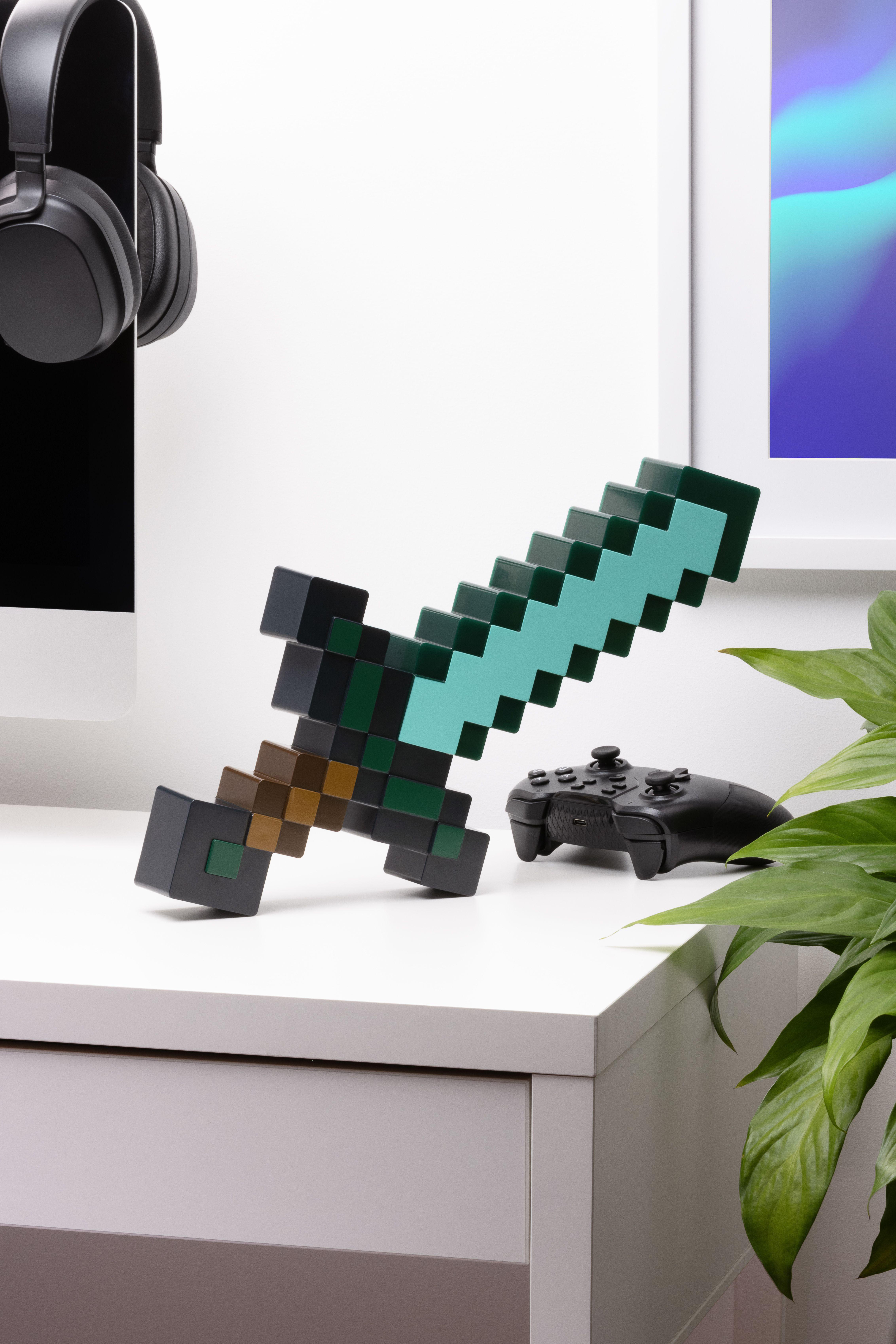 Ein pixeliges Schwert, ein schwarzer Gamecontroller und Kopfhörer auf einem weißen Schreibtisch.