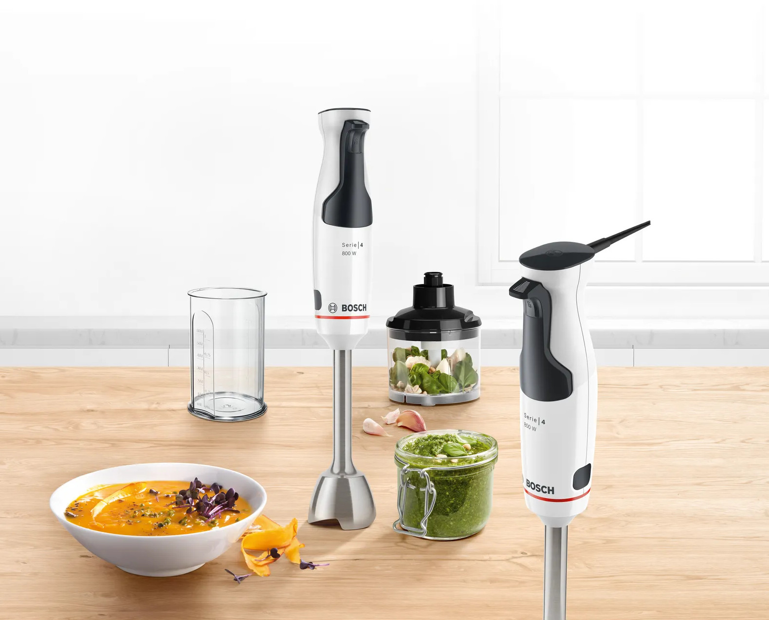 Blendery zanurzeniowe Bosch Serie 4 i akcesoria na drewnianej powierzchni, z produktami spożywczymi.