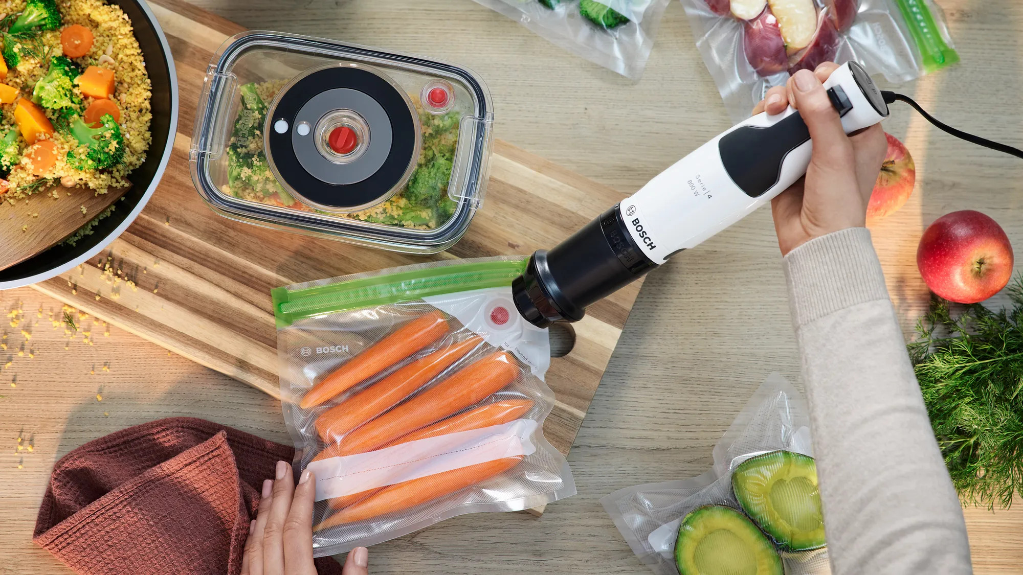 Osoba używająca białej i czarnej zgrzewarki próżniowej z produktami spożywczymi. Produkty znajdują się w plastikowych torbach.