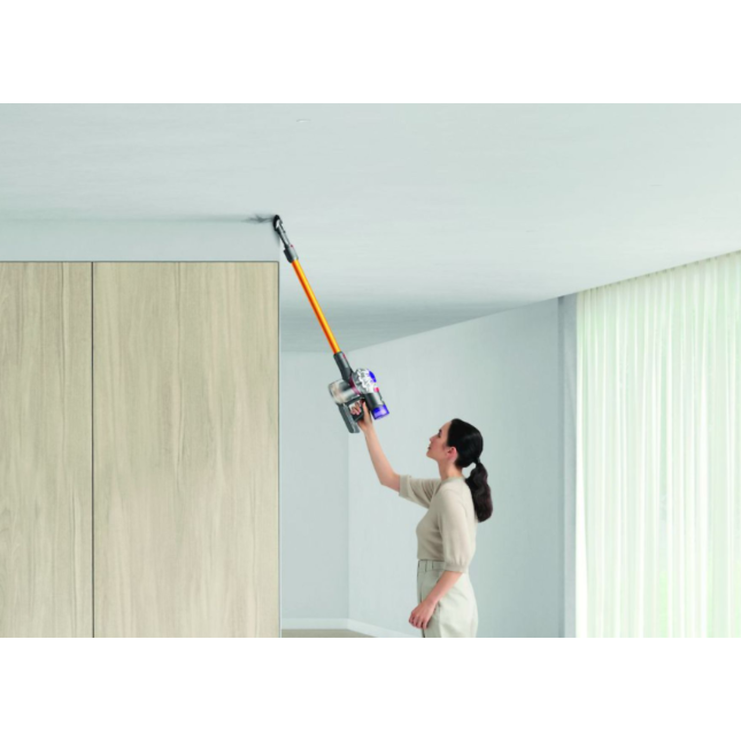 Vrouw stofzuigt plafond met een Dyson stofzuiger.
