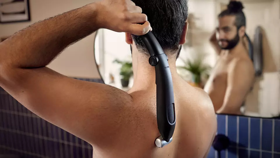 Mężczyzna goli plecy czarną golarką do pleców Philips, lustro w tle, otoczenie łazienki.