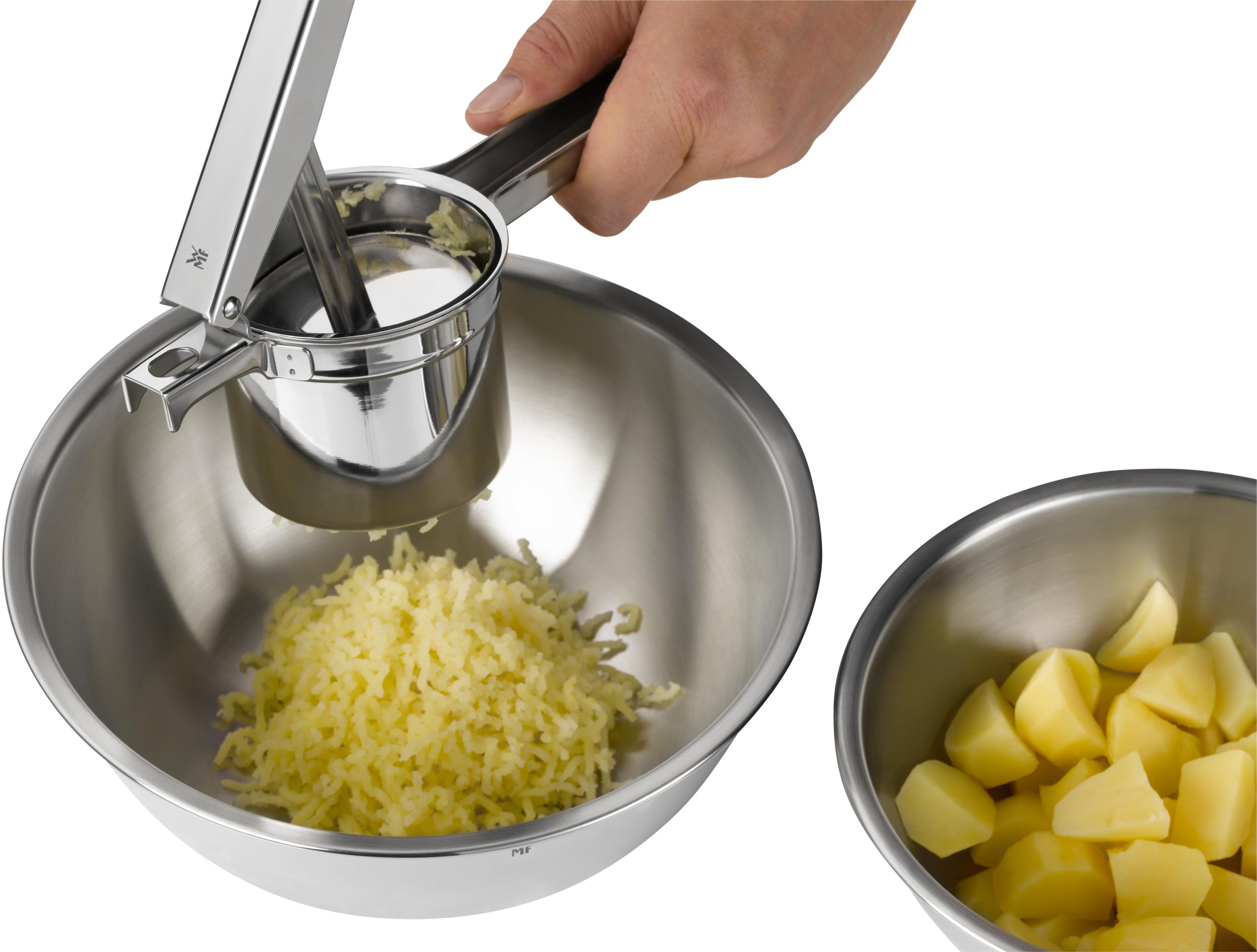 Eine Person, die einen Kartoffelstampfer über einer Schüssel mit Kartoffelpüree verwendet, neben einer Schüssel mit geschnittenen Kartoffeln.