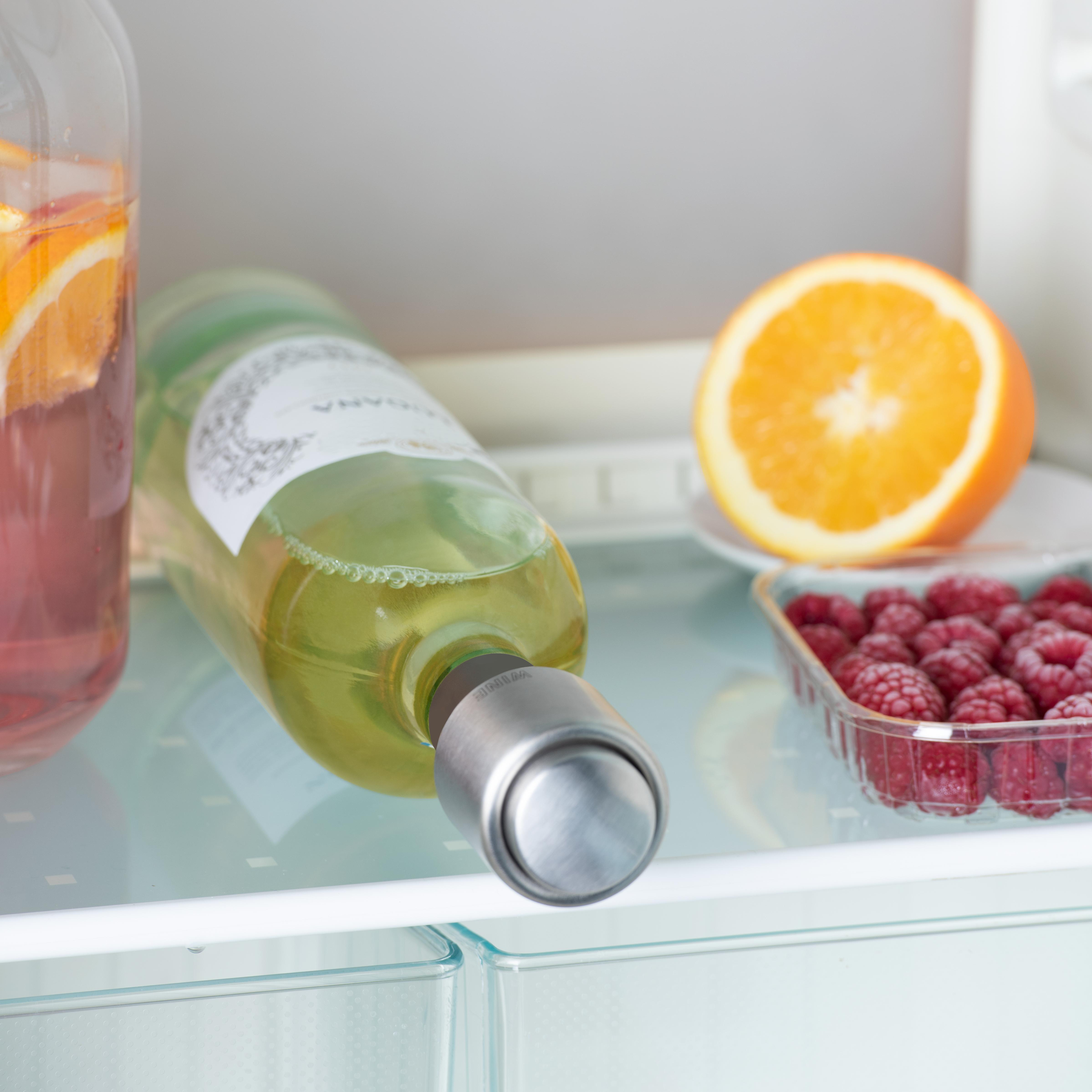 Eine Flasche Weißwein und eine Glasflasche mit Orangenscheiben auf einem Glasregal im Kühlschrank.