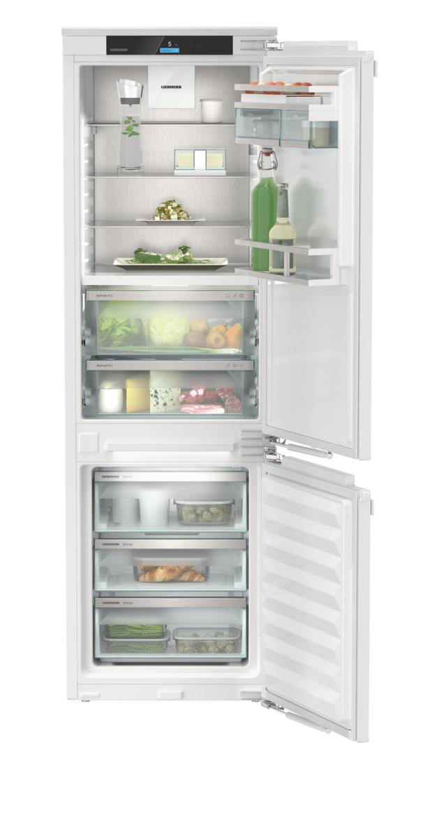 Weißer Einbau-Liebherr-Kühlschrank, Tür offen, zeigt Regale mit Lebensmitteln, Gemüse und Flaschen.