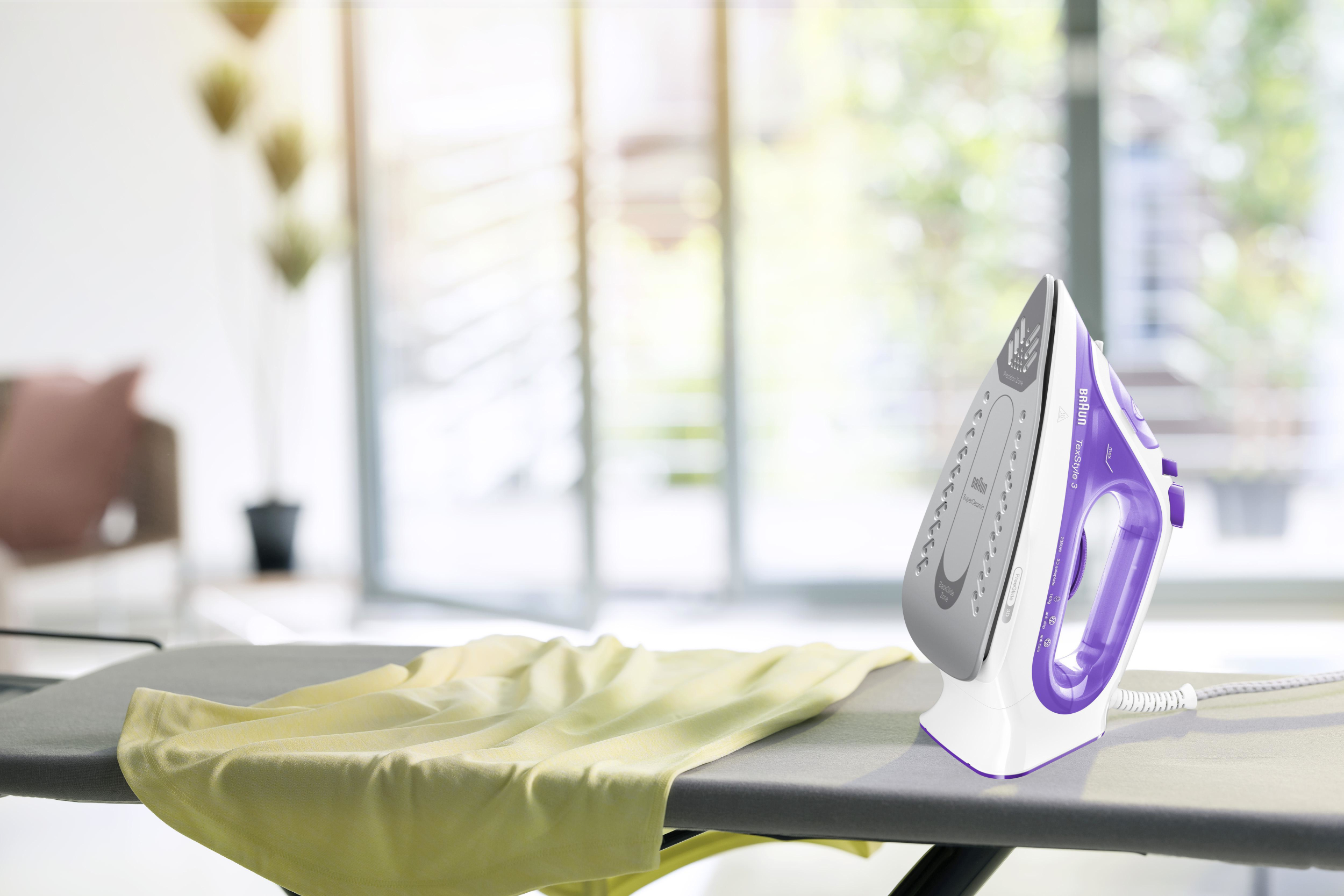 Żelazko z fioletowym uchwytem leży na desce do prasowania. Na desce jest żółty element garderoby.