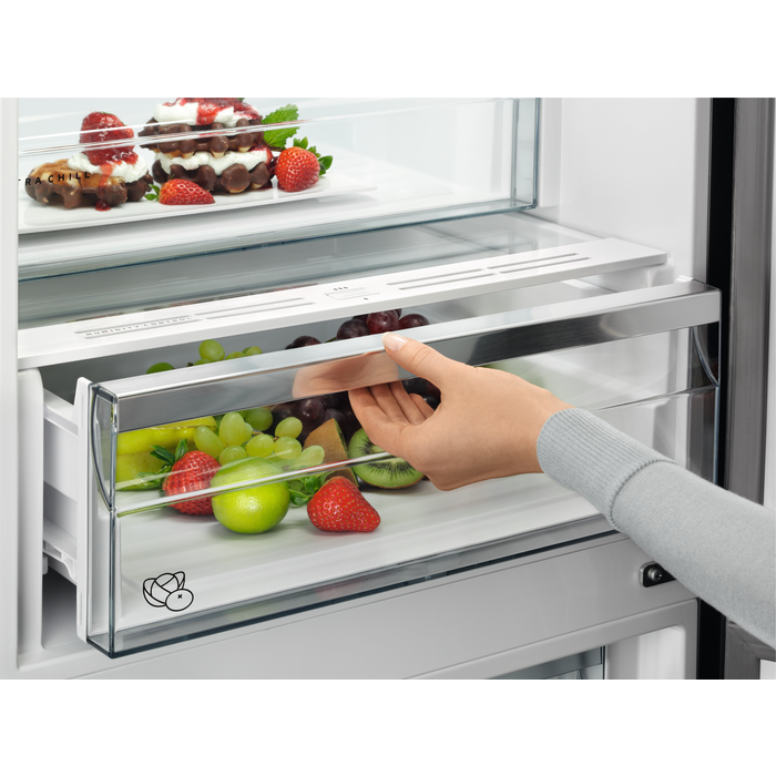 Egy kéz kinyit egy hűtőfiókot, tele gyümölcsökkel és zöldségekkel.