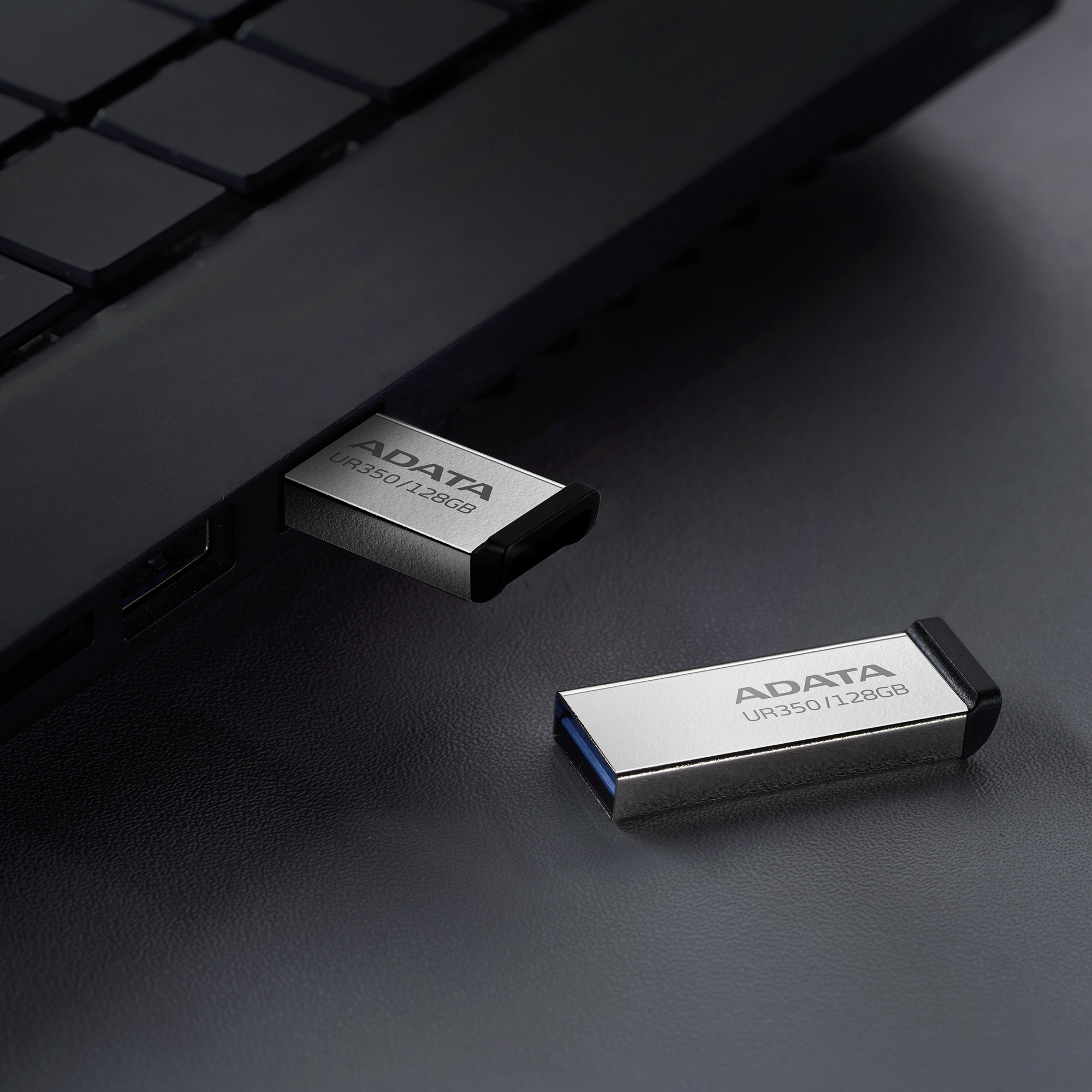 Két ezüst ADATA USB meghajtó egy fekete laptopba dugva és mellette.