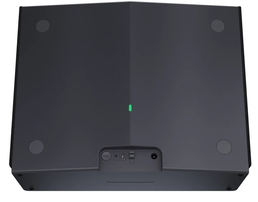 Widok od spodu ciemnoszarego urządzenia z okrągłymi nóżkami, zielonym światłem i portami.