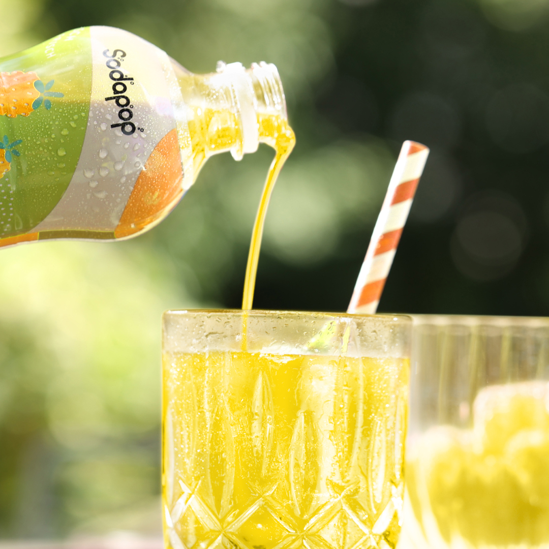 Eine Flasche gießt gelbe Limonade in ein Glas mit Eis und Strohhalm. Verschwommener grüner Hintergrund.