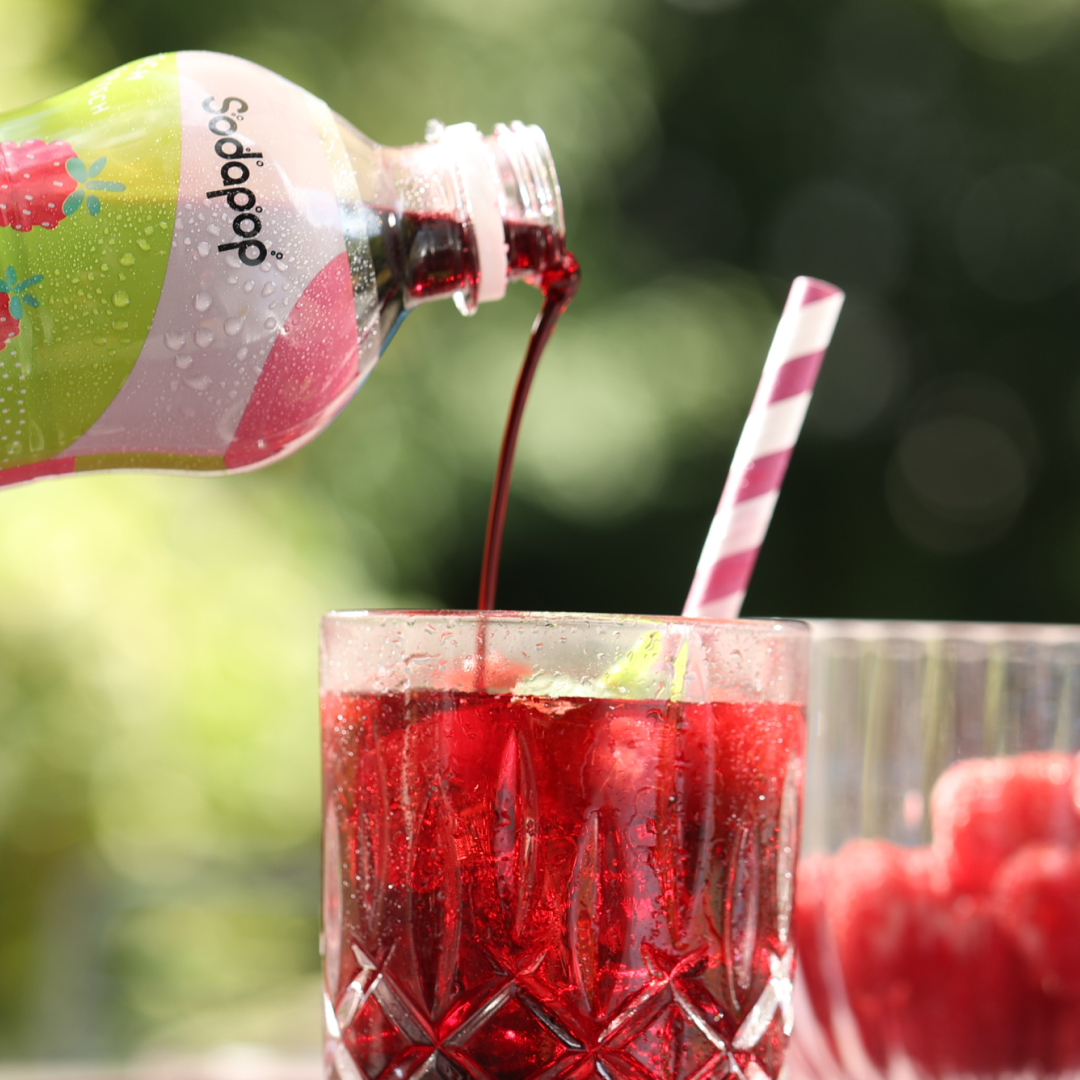 Rote Flüssigkeit, die aus einer Flasche in ein Glas mit Eis und Strohhalm gegossen wird.
