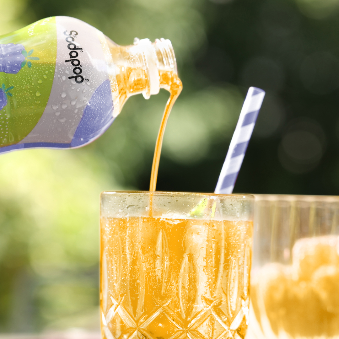 Eine Flasche gießt orangefarbene Limonade in ein Glas mit Strohhalm. Verschwommener grüner Hintergrund.