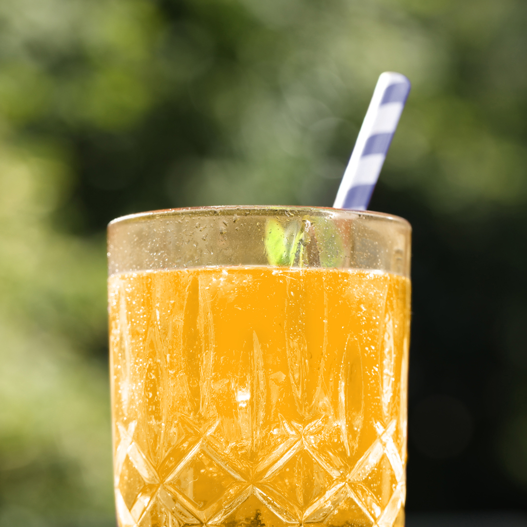 Orangenes Getränk in einem gemusterten Glas mit gestreiftem Strohhalm, Bokeh-Hintergrund.
