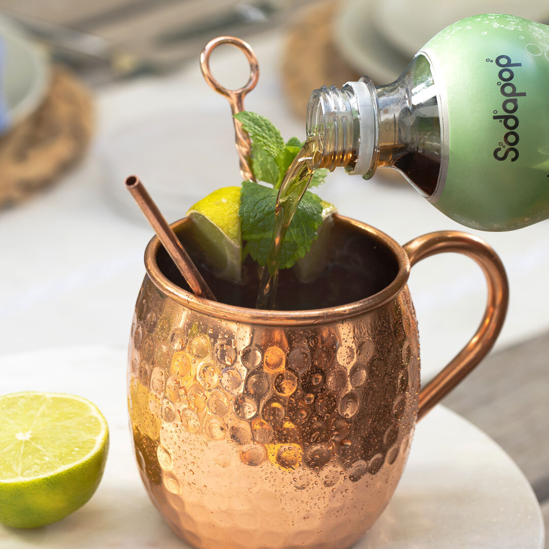 Cocktail wird in einen Kupferbecher mit Limette, Minze und Strohhalm gegossen, Nahaufnahme.